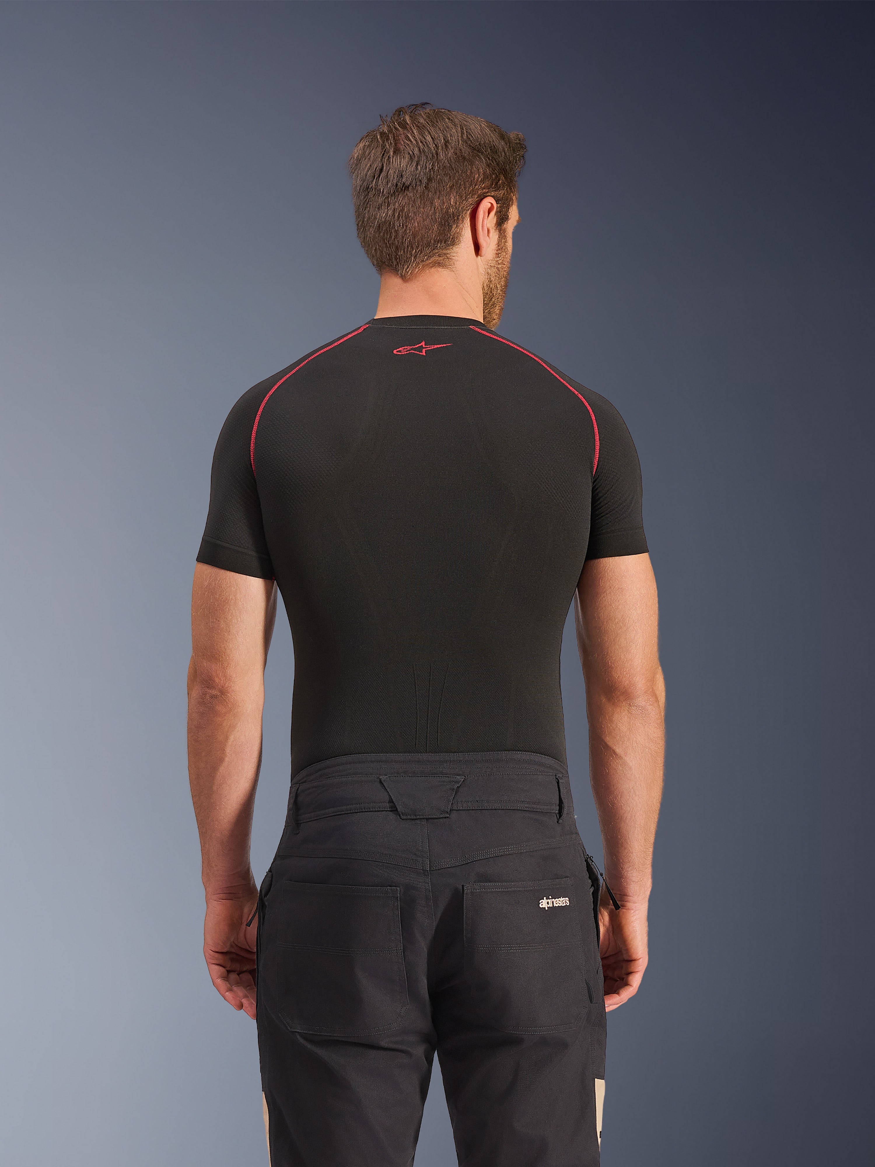 Alpinestars Flex-AST Canvas bukser i Black Aluminum, set bagfra på model, arbejdstøjsinspirerede urban motorcykelbukser med logo på baglommen, kombineret med et sort kortærmet basislag med røde syninger.