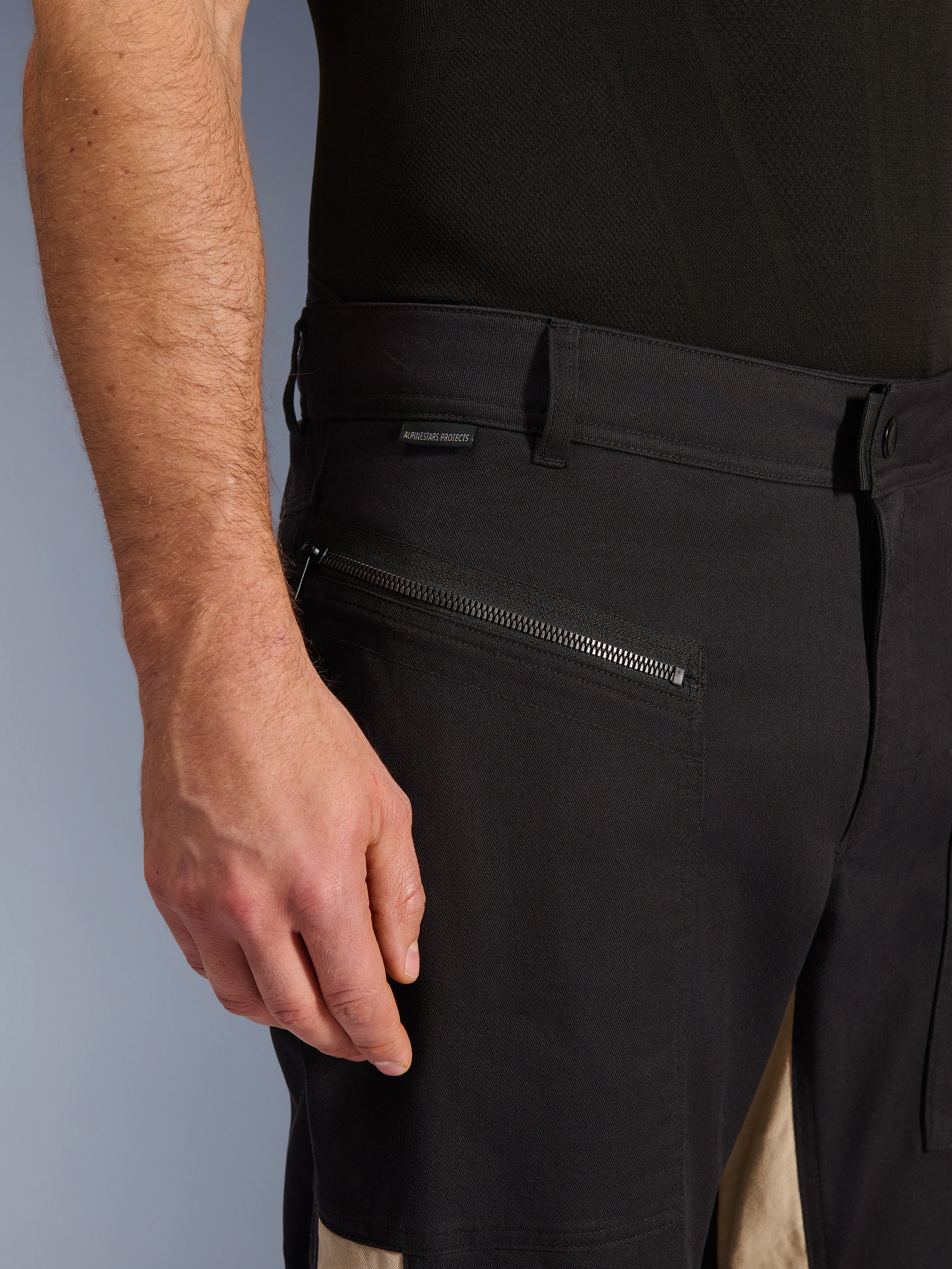 Alpinestars Flex-AST Canvas bukser i Black Aluminum, nærbillede af hofteområdet med en vandret kørelomme med lynlås, bæltestropper og lille mærkelogo, holdbar stretch-polybomuldskonstruktion til bykørsel.