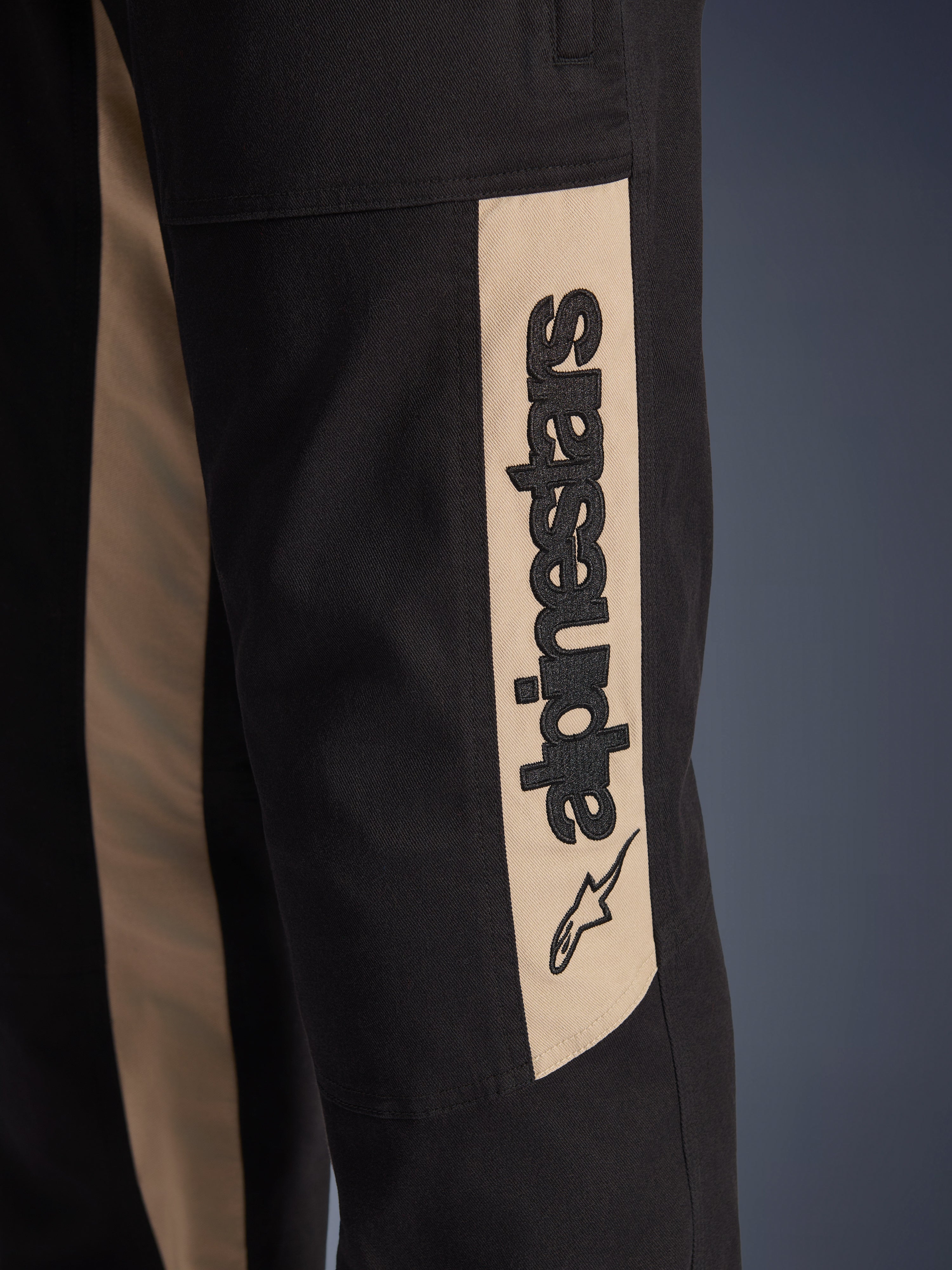 Alpinestars Flex-AST Canvas bukser, nærbillede af buksebenets side, sort med Aluminum accentpanel, lodret sort Alpinestars-logo og stjerne-ikon, slidstærkt polybomulds-twill til motorcykelkørsel i byen