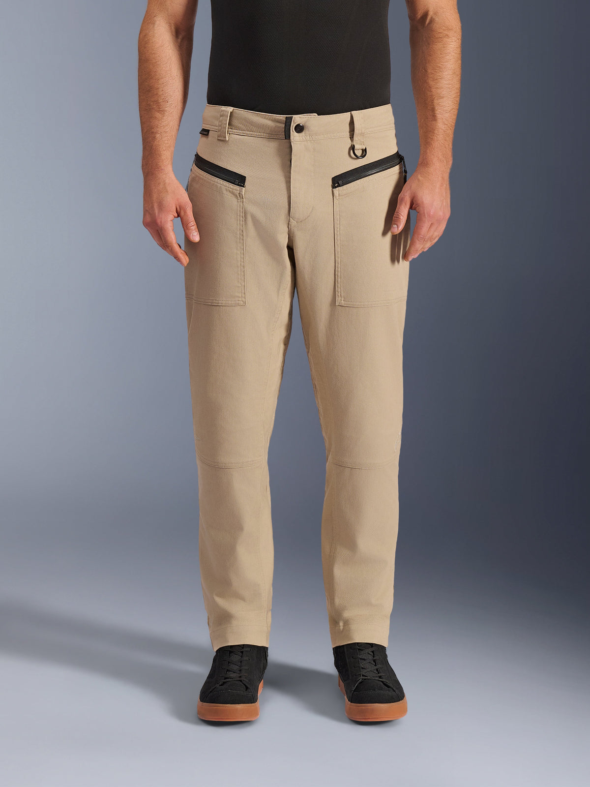 Alpinestars Flex-AST Canvas bukser, urban motorcykelbukser, brune, heritage arbejdstøjs-styling, med sorte horisontale forlommer med lynlås og D-ring i bæltestrop, båret med sort trøje og sko, studiebillede set forfra