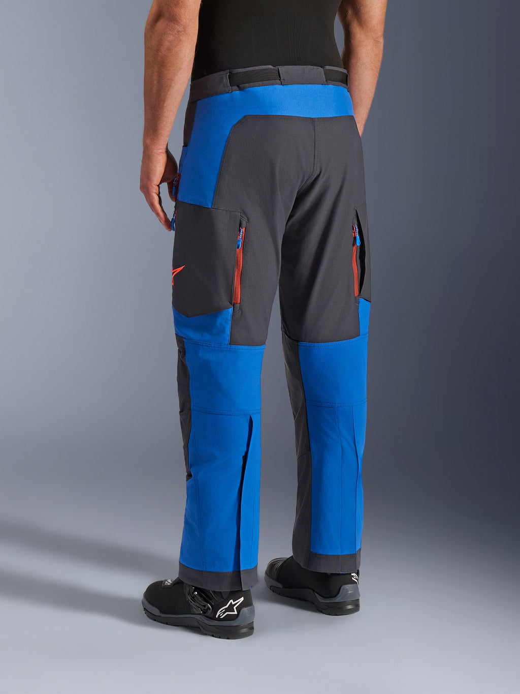 Alpinestars Maxdura Dual bukser, kongeblå og mørkegrå, set bagfra viser lynlåslommer og ventilationszoner, over-støvle design båret med sorte Alpinestars støvler, slidstærkt adventure- og dual-sport køreudstyr