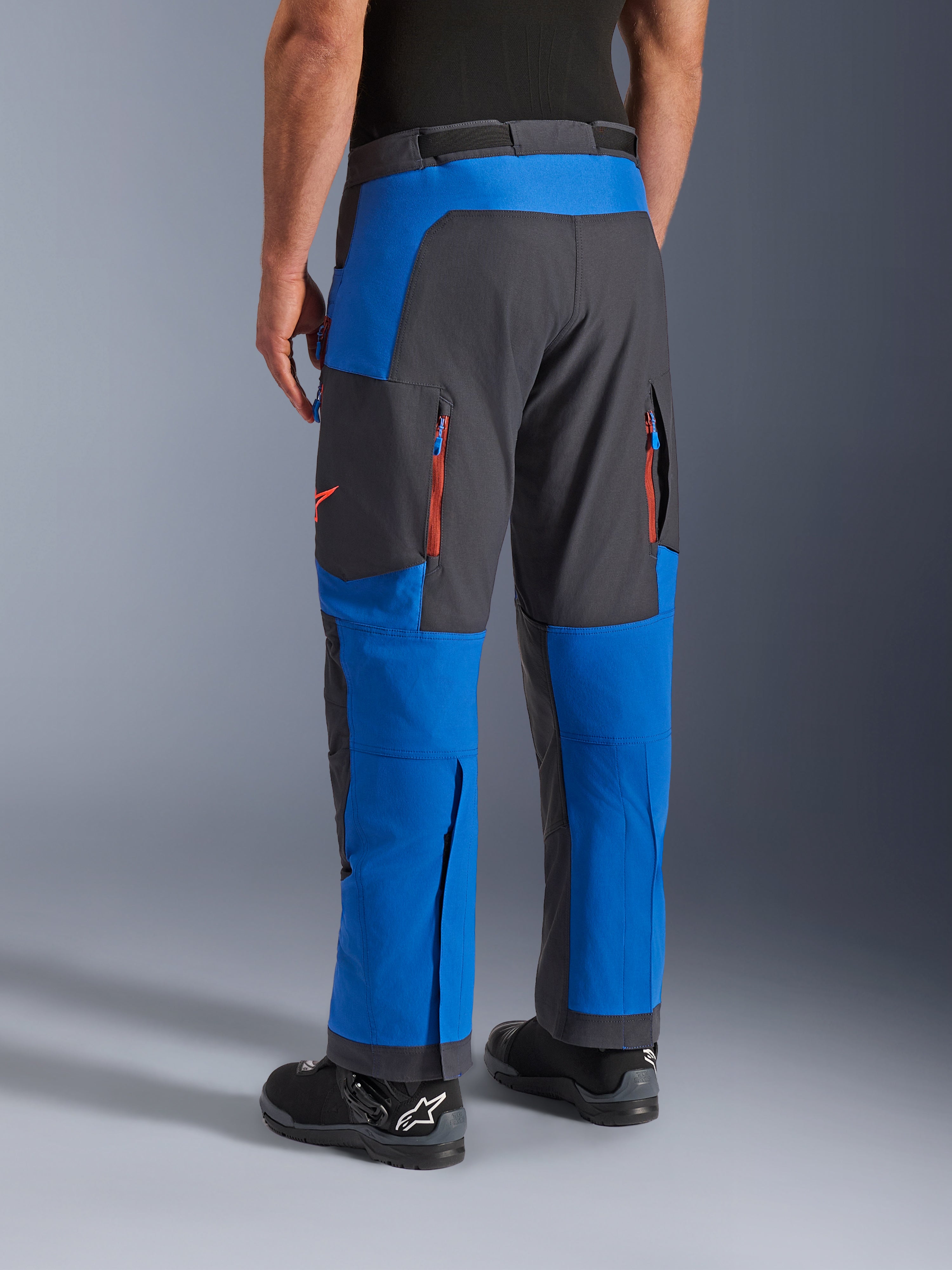 Alpinestars Maxdura Dual bukser, kongeblå og mørkegrå, set bagfra viser lynlåslommer og ventilationszoner, over-støvle design båret med sorte Alpinestars støvler, slidstærkt adventure- og dual-sport køreudstyr