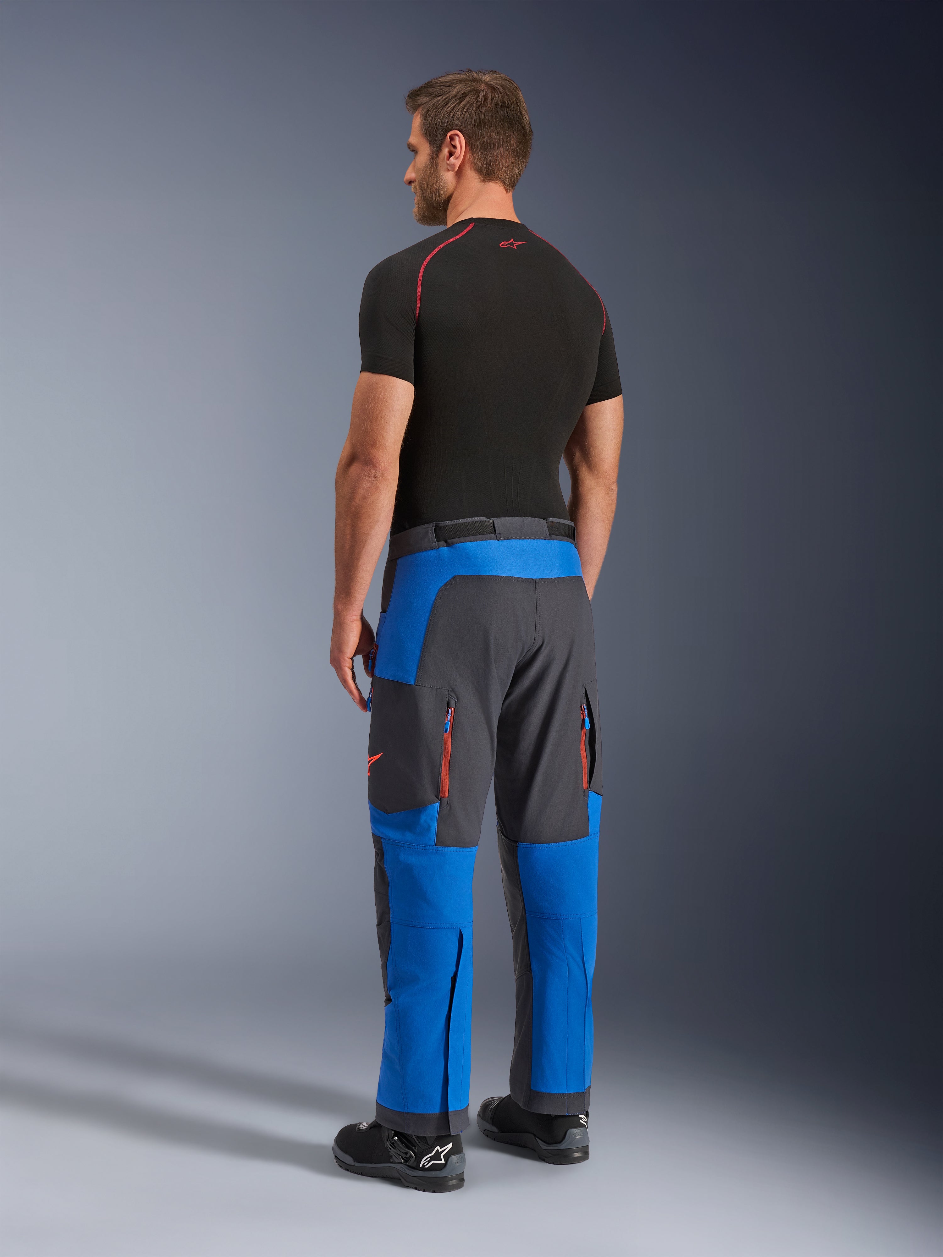Alpinestars Maxdura Dual bukser, adventure motorcykelbukser, kongeblå og mørkegrå, set bagfra på en model, orange ventilationsåbninger med lynlås, over-støvle adventure-pasform, holdbart stretchmateriale