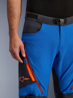 Alpinestars Maxdura Dual bukser i kongeblå og mørkegrå, nærbillede af linningen med magnetspænde, lynlåslomme med orange detaljer og rødt Alpinestars-logo, teknisk adventure-motorcykeludstyr