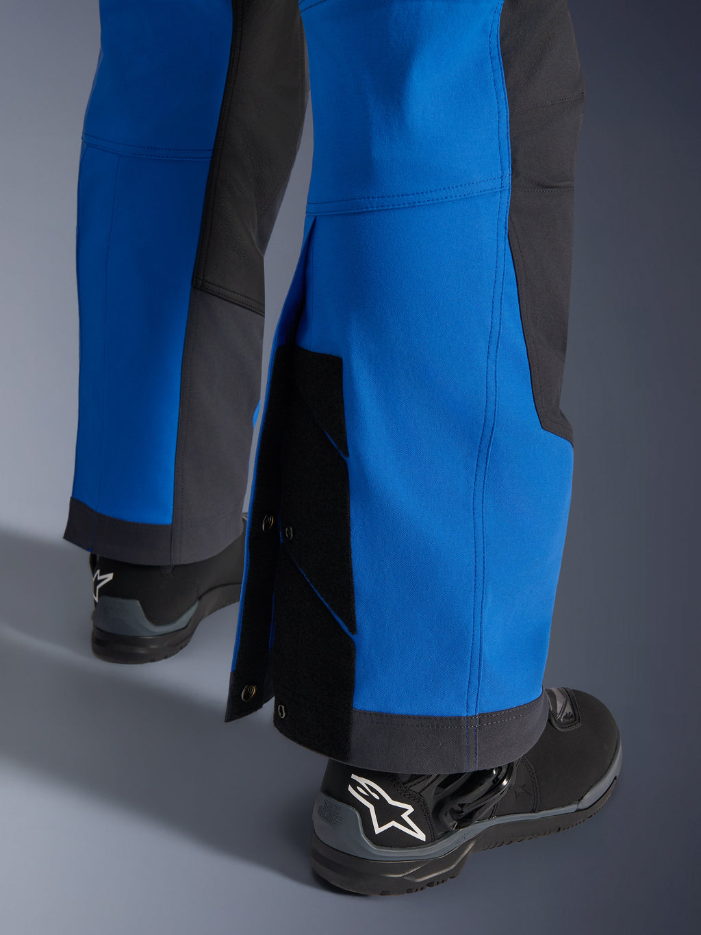 Alpinestars Maxdura Dual bukser, Royal Blue og Deep Gray, nærbillede af justerbart nederste bukseben med tryklåse og kile, over-støvle adventure-pasform, båret med sorte Alpinestars motorcykelstøvler