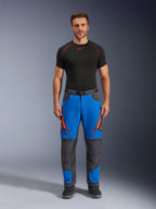 Alpinestars Maxdura Dual bukser, adventure-motorcykelbukser, kongeblå og mørkegrå, orange lynlåsdetaljer, bæres med et sort Alpinestars-basislag og sorte støvler, med forstærkede knæpaneler og et teknisk off-road-design