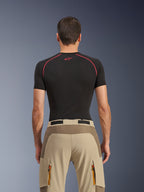 Alpinestars Maxdura Dual bukser, adventure-motorcykelbukser, Walnut Aluminum, set bagfra med forstærket sædepanel og beige stretch-stof, cargolommer med lynlås og orange stropper, båret med en sort Alpinestars base layer-trøje.