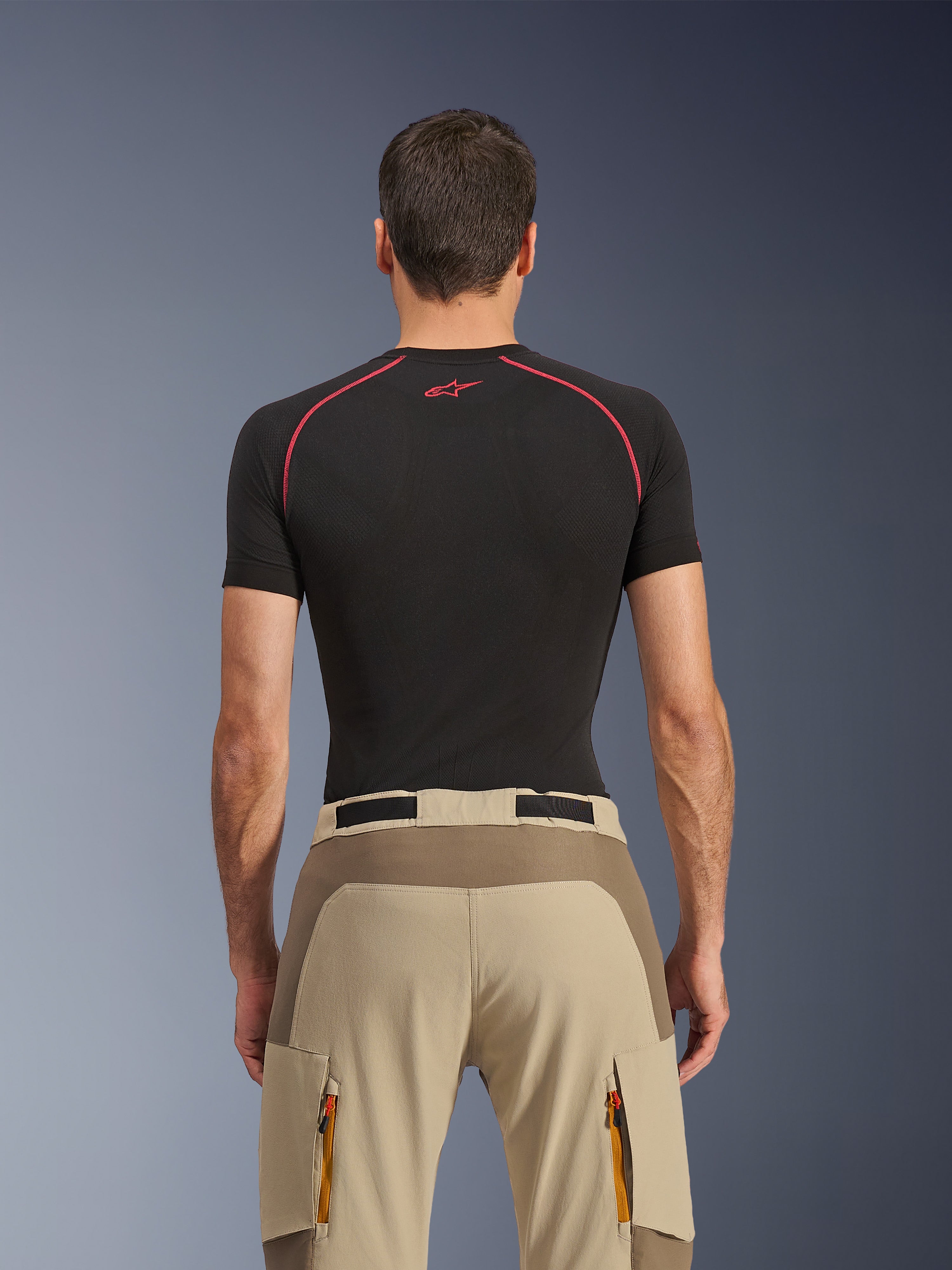 Alpinestars Maxdura Dual bukser, adventure-motorcykelbukser, Walnut Aluminum, set bagfra med forstærket sædepanel og beige stretch-stof, cargolommer med lynlås og orange stropper, båret med en sort Alpinestars base layer-trøje.