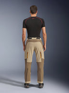 Alpinestars Maxdura Dual bukser i Walnut Aluminum, set bagfra, tofarvet brunt og beige design, adventure-kørebukser med cargolommer med lynlås og forstærket sæde, båret med en sort kompressionstrøje og motorcykelstøvler.