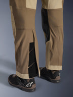 Alpinestars Maxdura Dual bukser i Walnut Aluminum, detaljeret visning af underbenet og sømmen med over-støvle-design, justerbare burrelukninger og forstærkede inderpaneler, kombineret med sorte motorcykelstøvler.