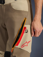 Alpinestars Maxdura Dual bukser, Walnut og Aluminum, nærbillede af lårdetalje med et stort diagonalt ventilationssystem med lynlås og røde detaljer, rødt Alpinestars-logo på et sandfarvet panel, adventure motorcykeludstyr