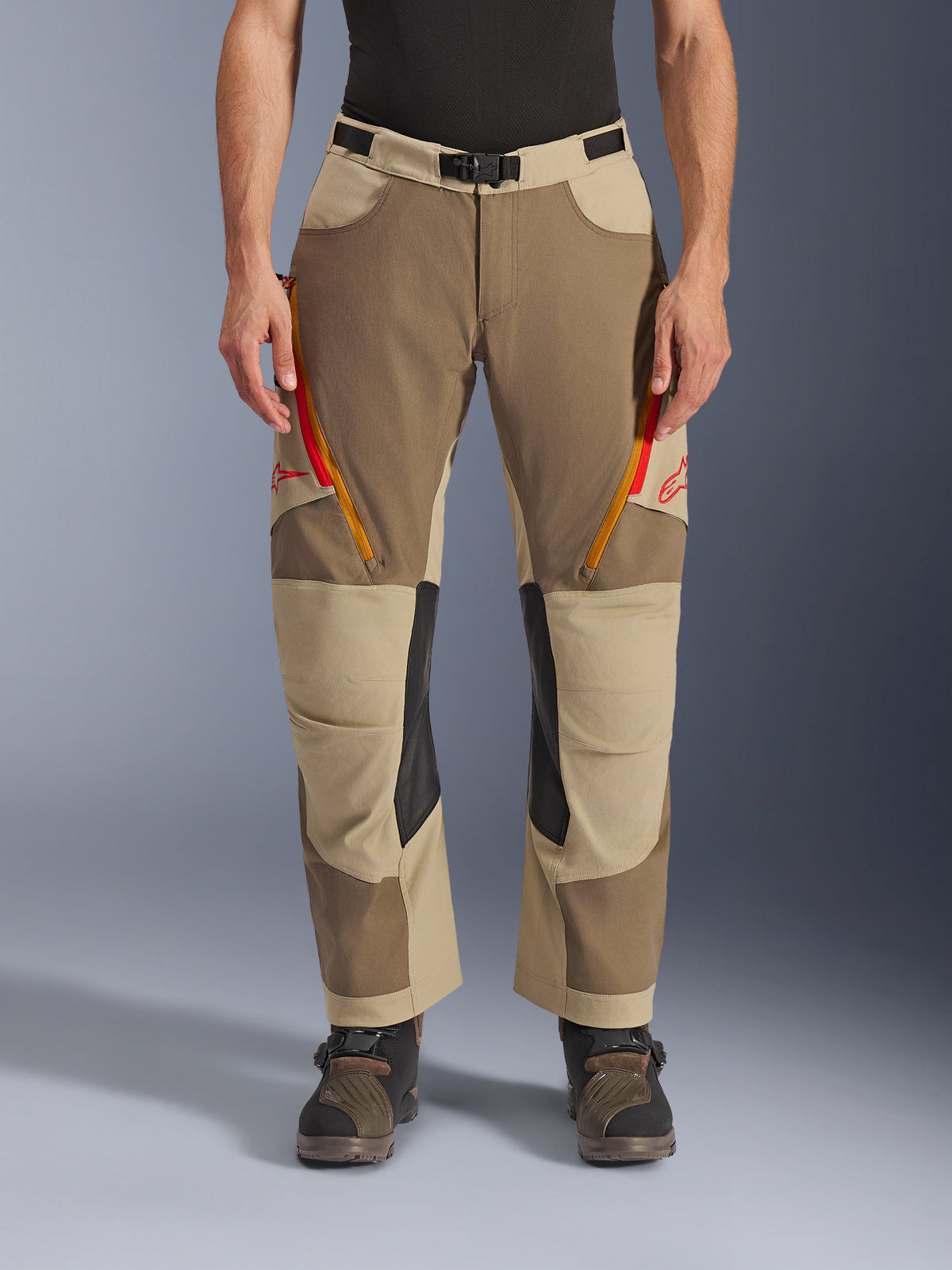 Alpinestars Maxdura Dual bukser, Walnut Aluminum, adventure motorcykelbukser med røde og orange lynlåsventilationsåbninger på lårene, sorte indvendige knæpaneler i læder, båret med et sort baselayer og robuste støvler, slidstærkt multitonalt design til dual-sport kørsel