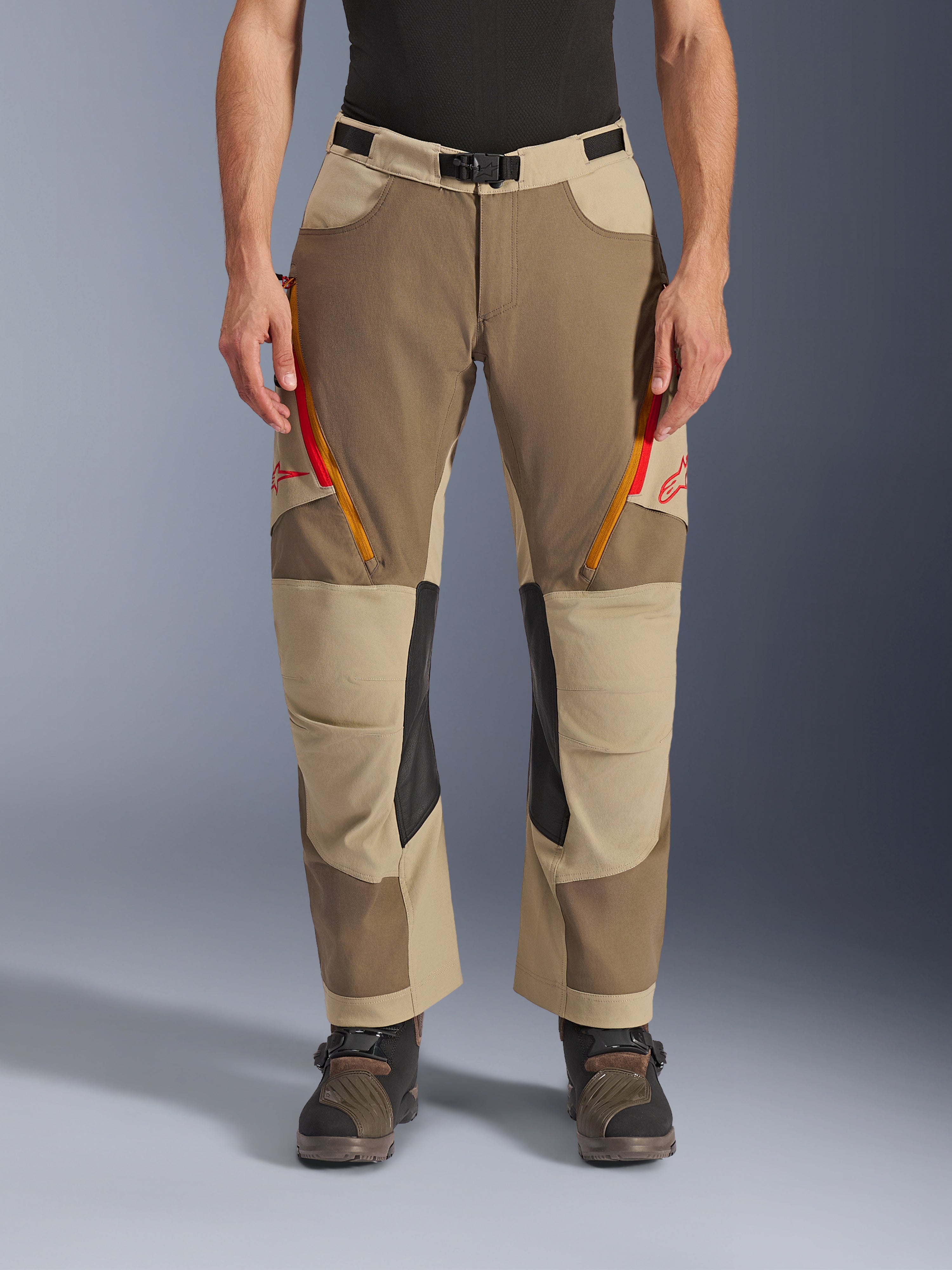 Alpinestars Maxdura Dual bukser, Walnut Aluminum, adventure motorcykelbukser med røde og orange lynlåsventilationsåbninger på lårene, sorte indvendige knæpaneler i læder, båret med et sort baselayer og robuste støvler, slidstærkt multitonalt design til dual-sport kørsel