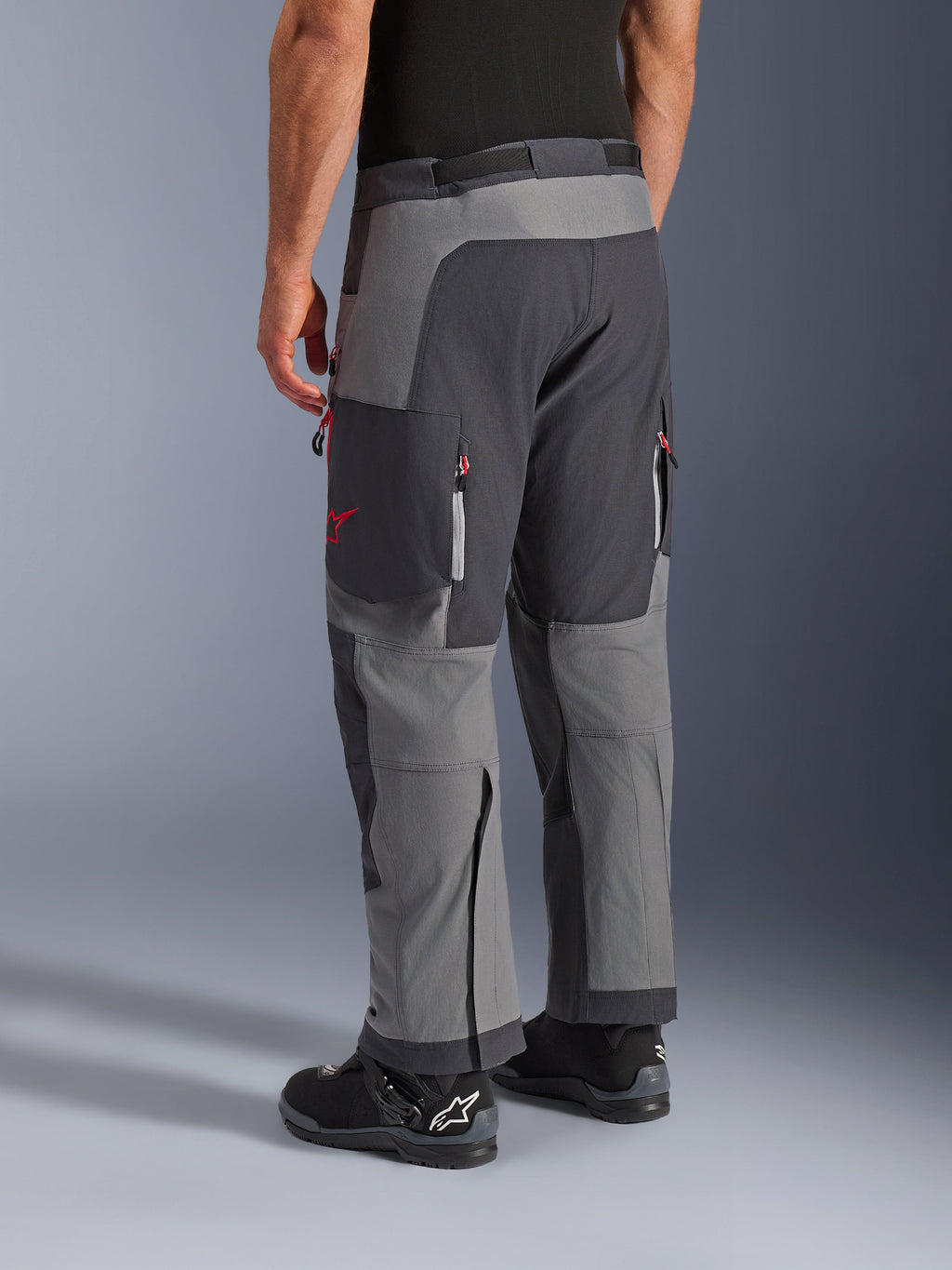 Alpinestars Maxdura Dual bukser, adventure motorcykelbukser, mørkegrå og dyb grå, set bagfra med multi-panel konstruktion, røde lynlåsdetaljer og stjernelogo, kombineret med sorte Alpinestars støvler, designet til dual-sport ydeevne
