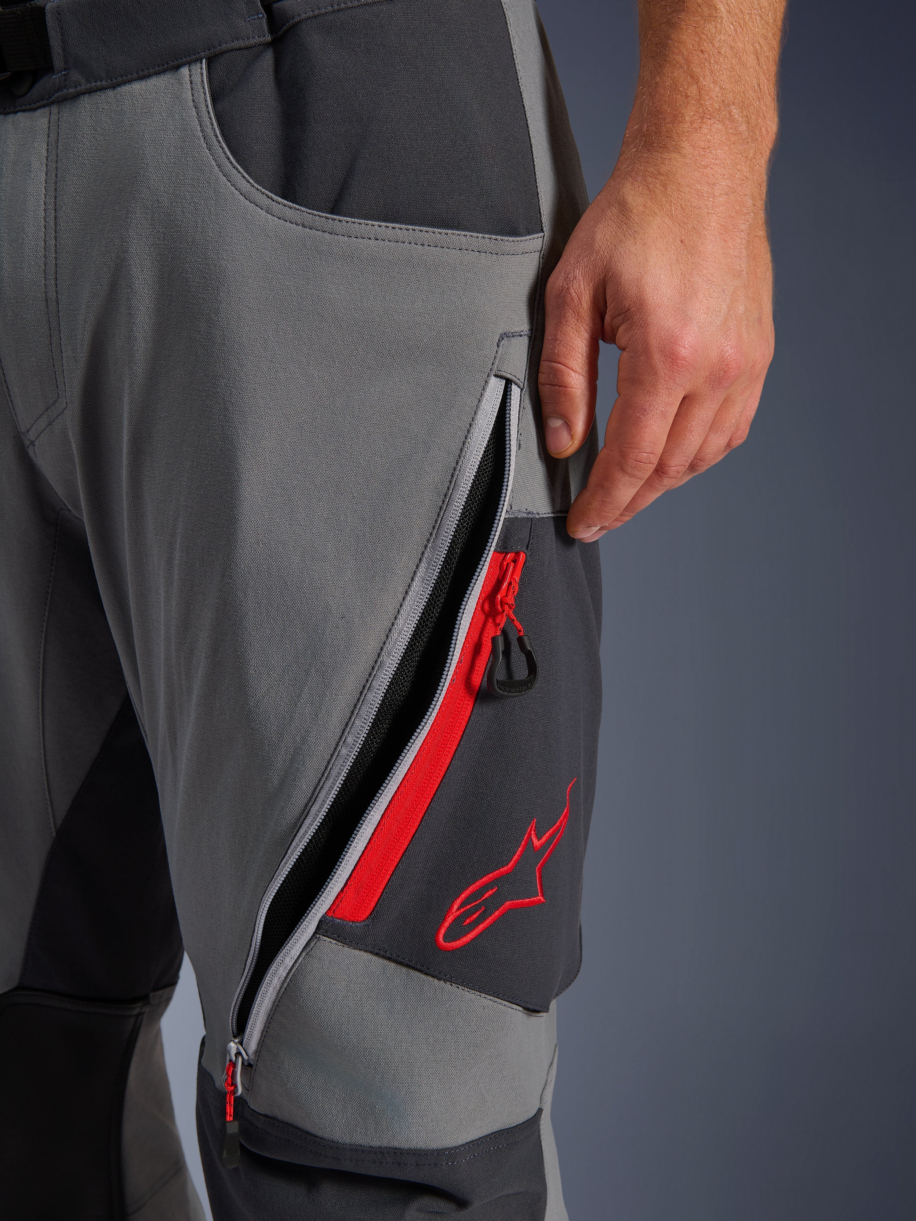 Alpinestars Maxdura Dual bukser, mørkegrå og Deep Gray adventure motorcykelbukser, nærbillede af åben lårventilation med lynlås, røde detaljer og broderet rødt stjernelogo, teknisk strækstofdesign