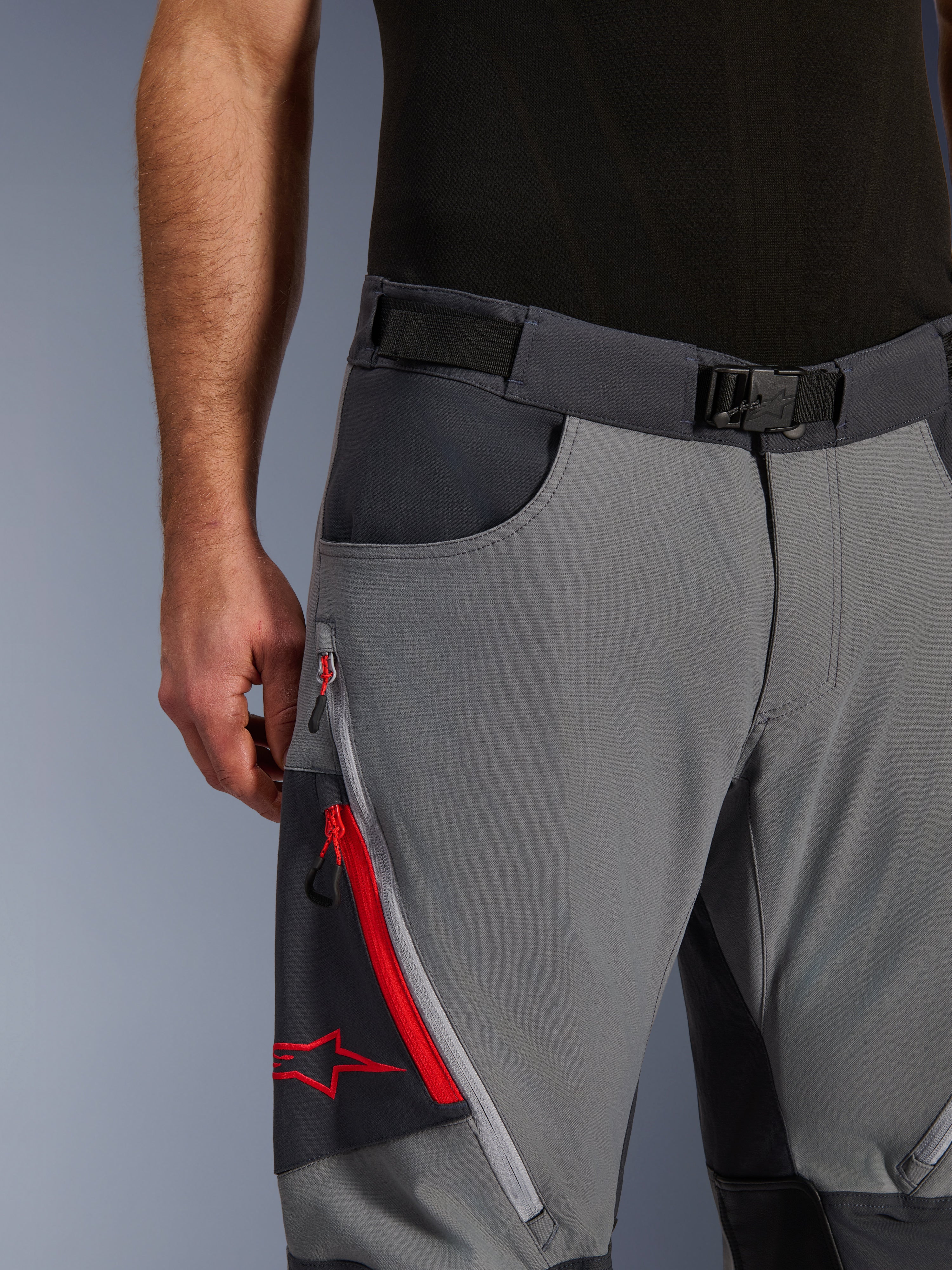 Alpinestars Maxdura Dual bukser, adventure motorcykelbukser, mørkegrå og dyb grå, nærbillede med justerbart taljebælte med magnetisk spænde, cargolomme med lynlås med røde detaljer og Alpinestars-logo.