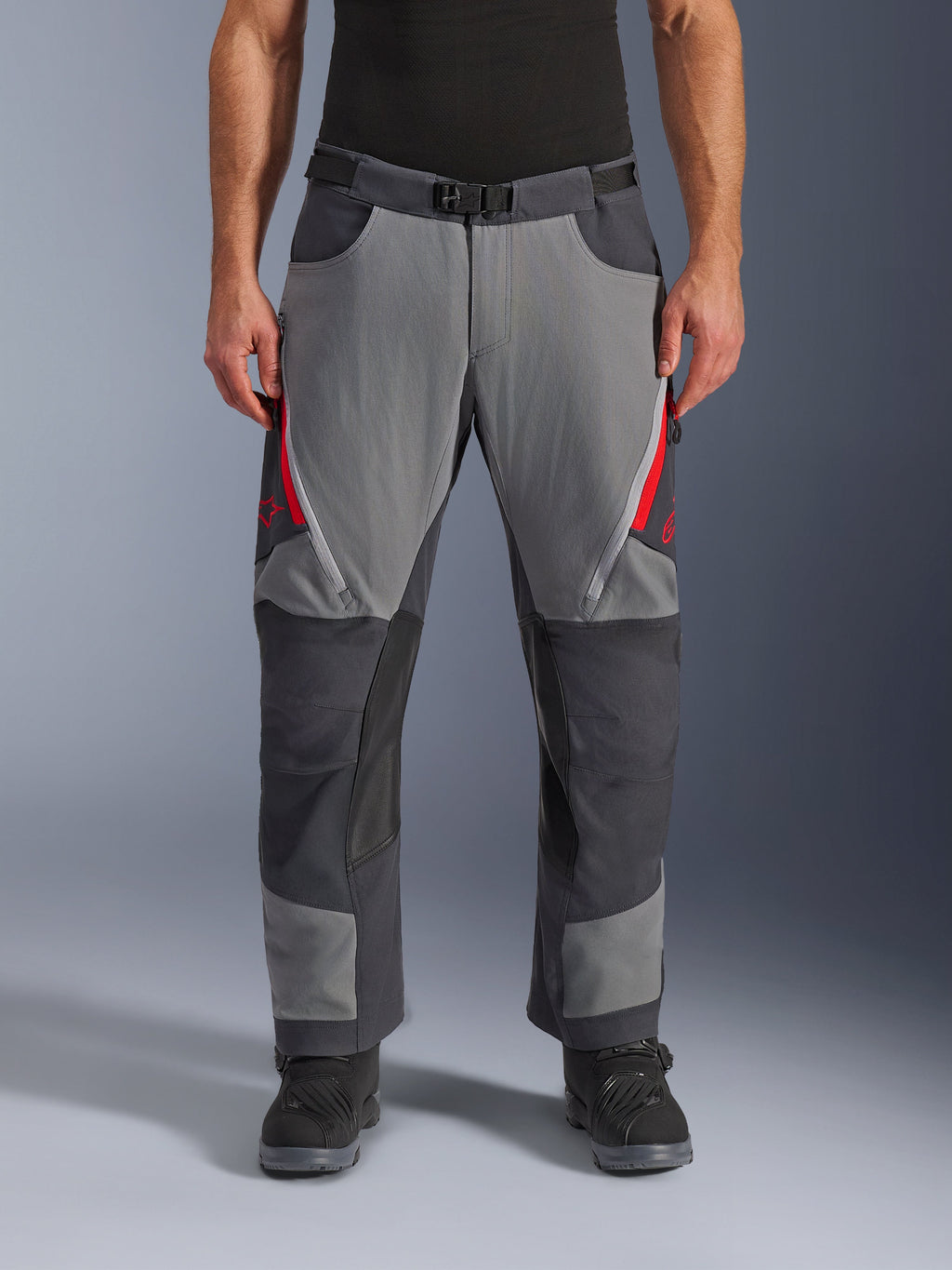 Alpinestars Maxdura Dual bukser, adventure motorcykelbukser, mørkegrå og dyb grå med røde detaljer, set forfra med lynlåsåbninger på lårene, magnetisk spændebælte og forstærkede knæpaneler, over-støvle design til dual-sport kørsel.