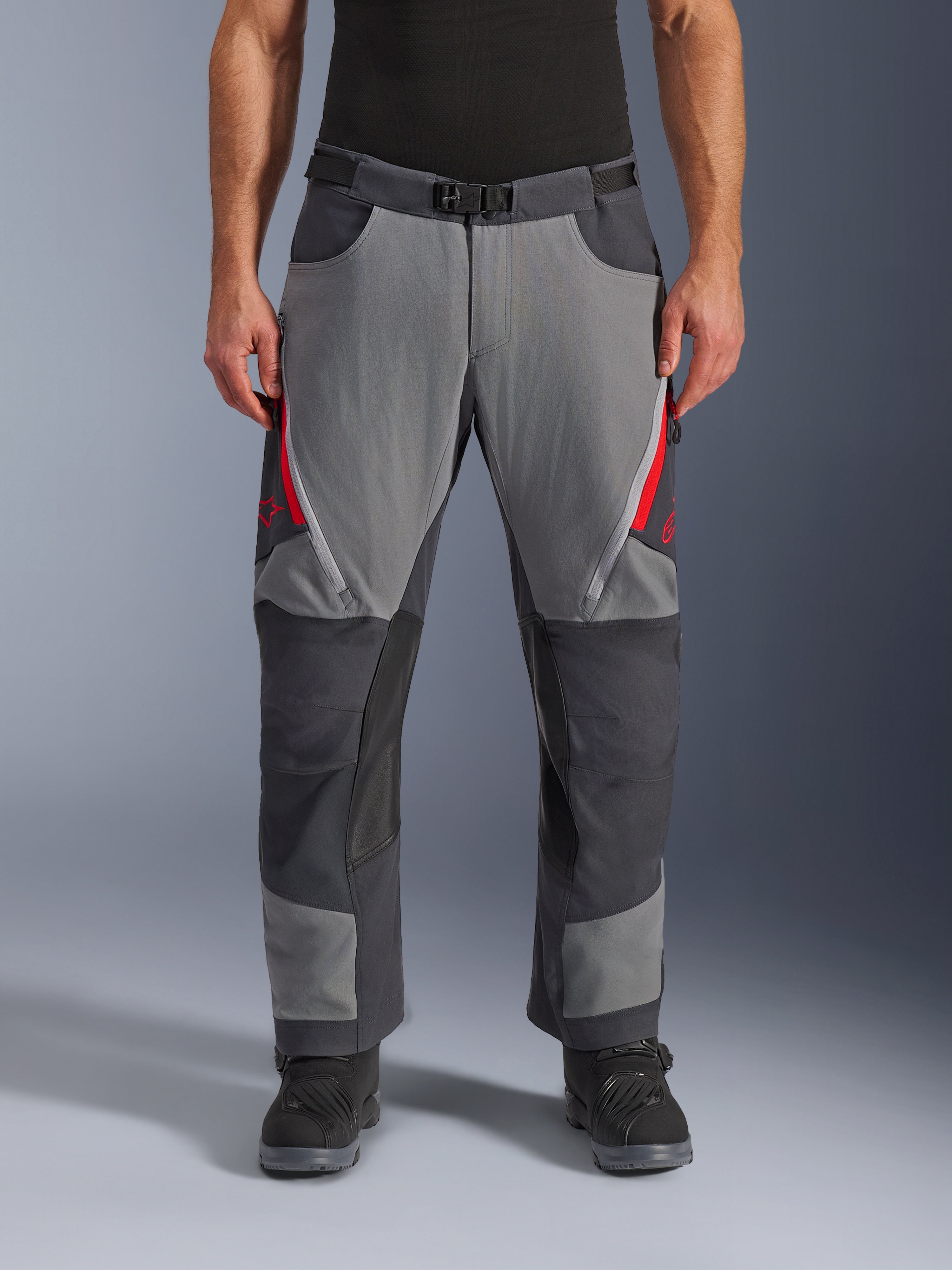 Alpinestars Maxdura Dual bukser, adventure motorcykelbukser, mørkegrå og dyb grå med røde detaljer, set forfra med lynlåsåbninger på lårene, magnetisk spændebælte og forstærkede knæpaneler, over-støvle design til dual-sport kørsel.