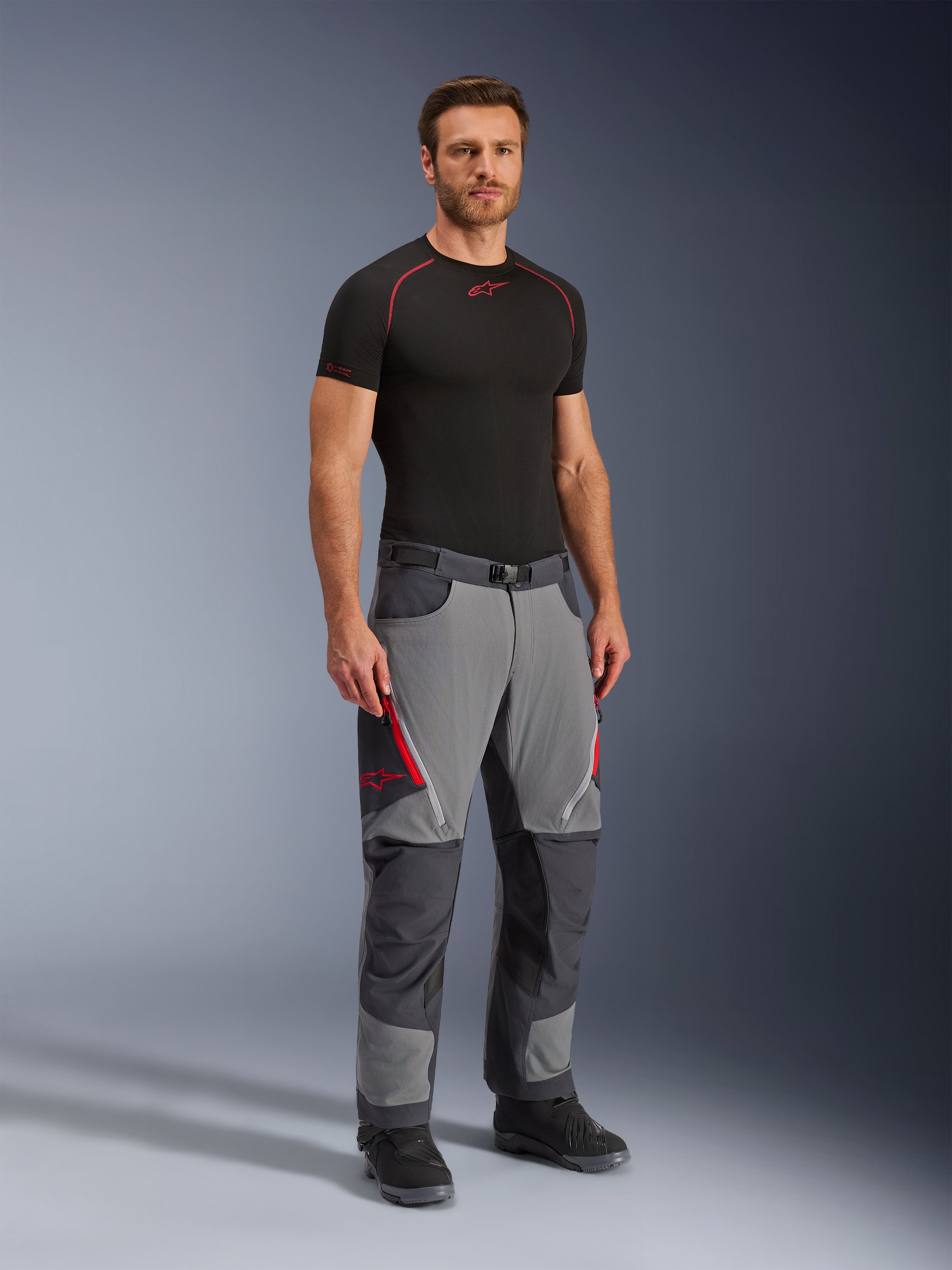 Alpinestars Maxdura Dual Pants, adventure motorcykelbukser, mørkegrå og dybgrå, bæres med et sort basislag og støvler, med røde ventilationsåbninger med lynlås, forstærkede paneler på knæ og sæde og en talje med bælte, atletisk pasform til dual-sport-kørsel