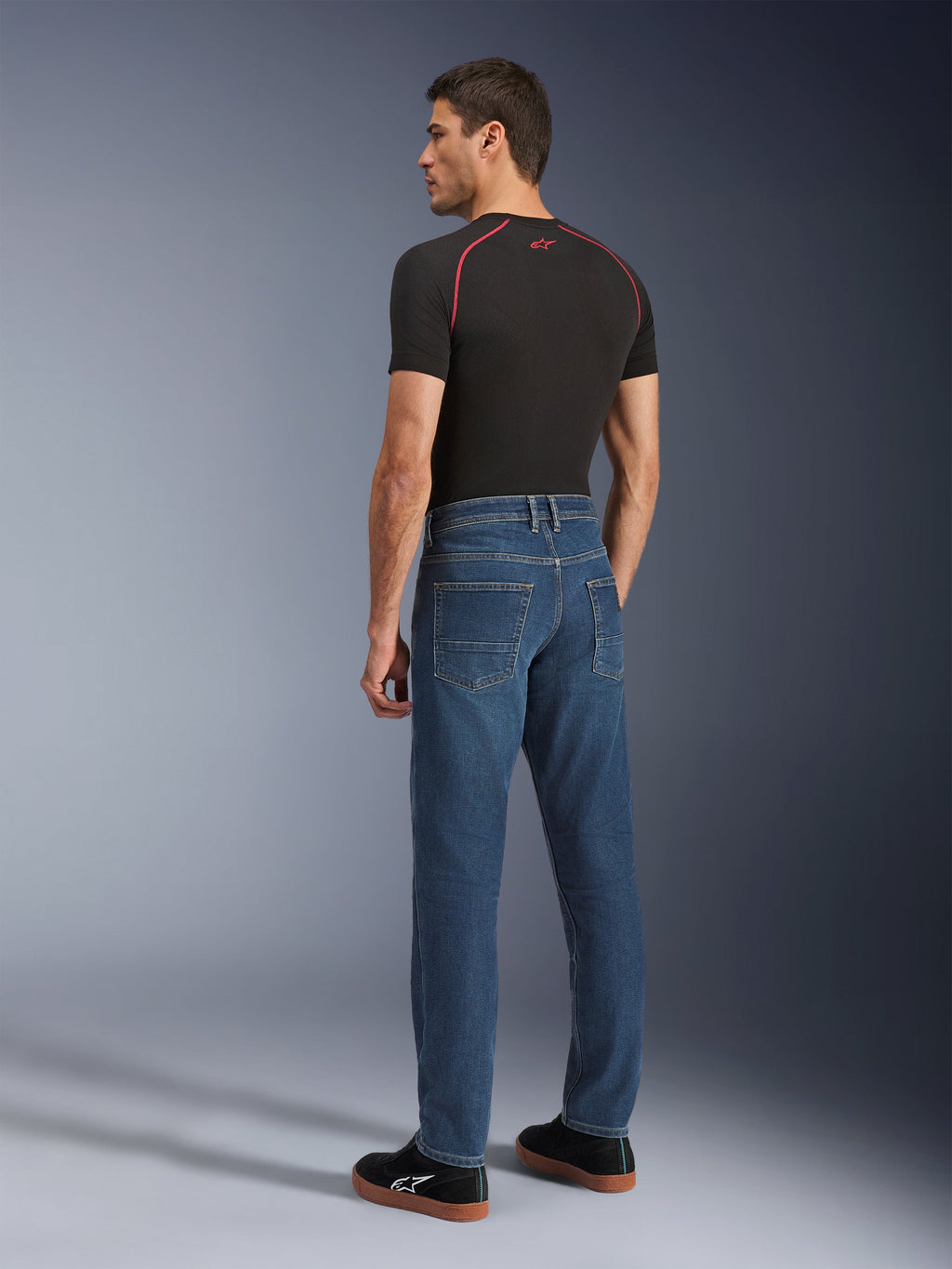 Alpinestars Flex-AST 5 Denim bukser, Indigo Washed, model set bagfra iført bukserne, urbane motorcykeljeans, afsmalnende pasform med monolags stretch denim, kombineret med en sort t-shirt og sorte sneakers