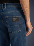 Alpinestars Flex-AST 5 Denim bukser, urbane motorcykeljeans, Indigo Washed, tærbillede af baglommen med en sort Alpinestars logo-patch med teksten 'One Goal. One Vision.', kontrastfarvede guldstikninger og monolags denimtekstur