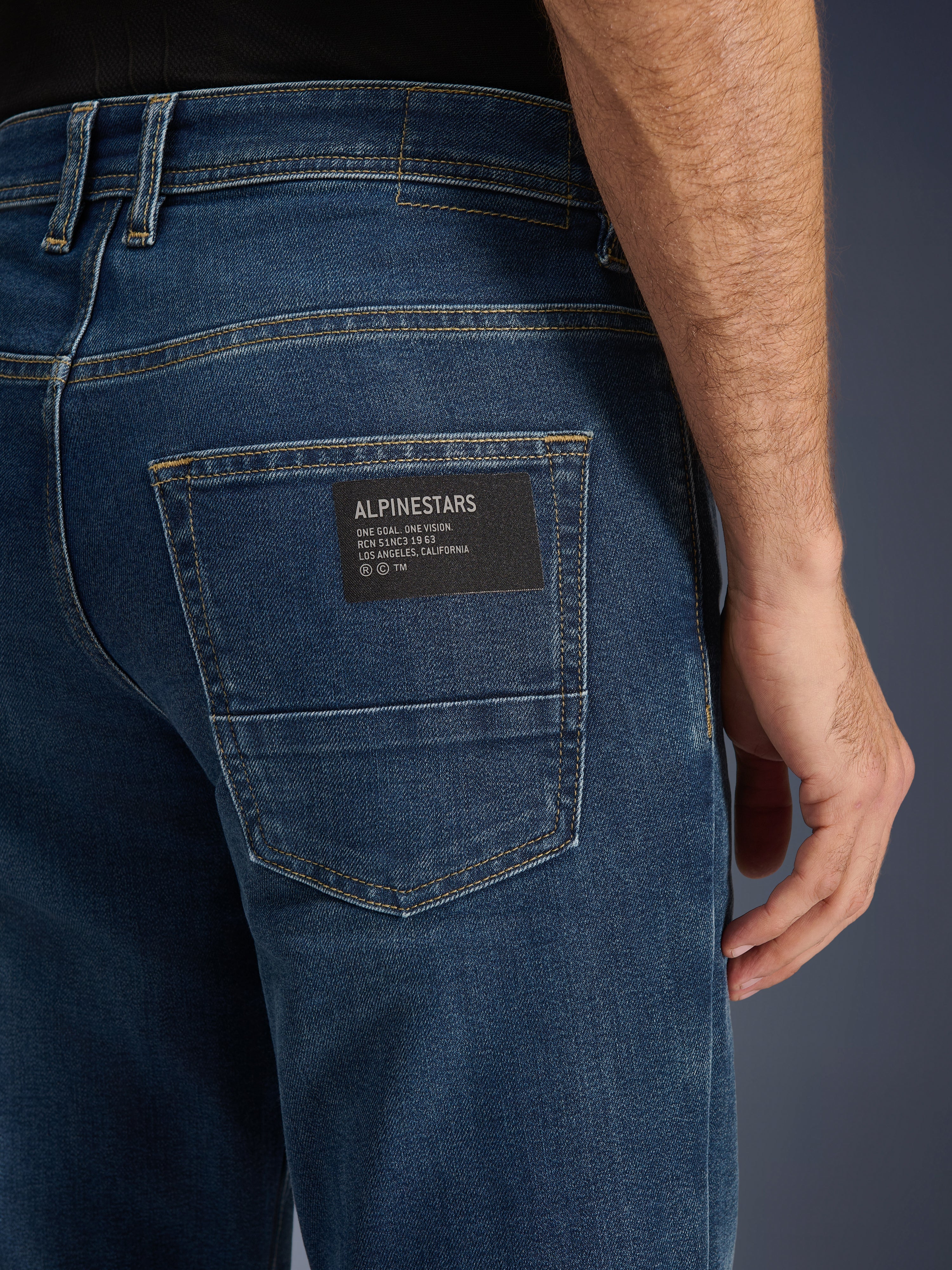 Alpinestars Flex-AST 5 Denim bukser, urbane motorcykeljeans, Indigo Washed, tærbillede af baglommen med en sort Alpinestars logo-patch med teksten 'One Goal. One Vision.', kontrastfarvede guldstikninger og monolags denimtekstur