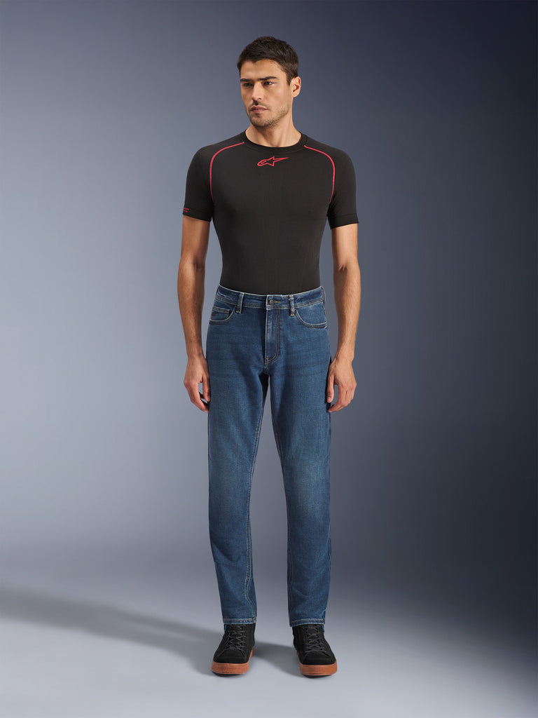 Alpinestars Flex-AST 5 Denim bukser, motorcykel-denimbukser, Indigo Washed, båret med en sort performance-t-shirt og sorte sneakers, med en tilspidset pasform og monolags stretch-denimkonstruktion til bykørsel