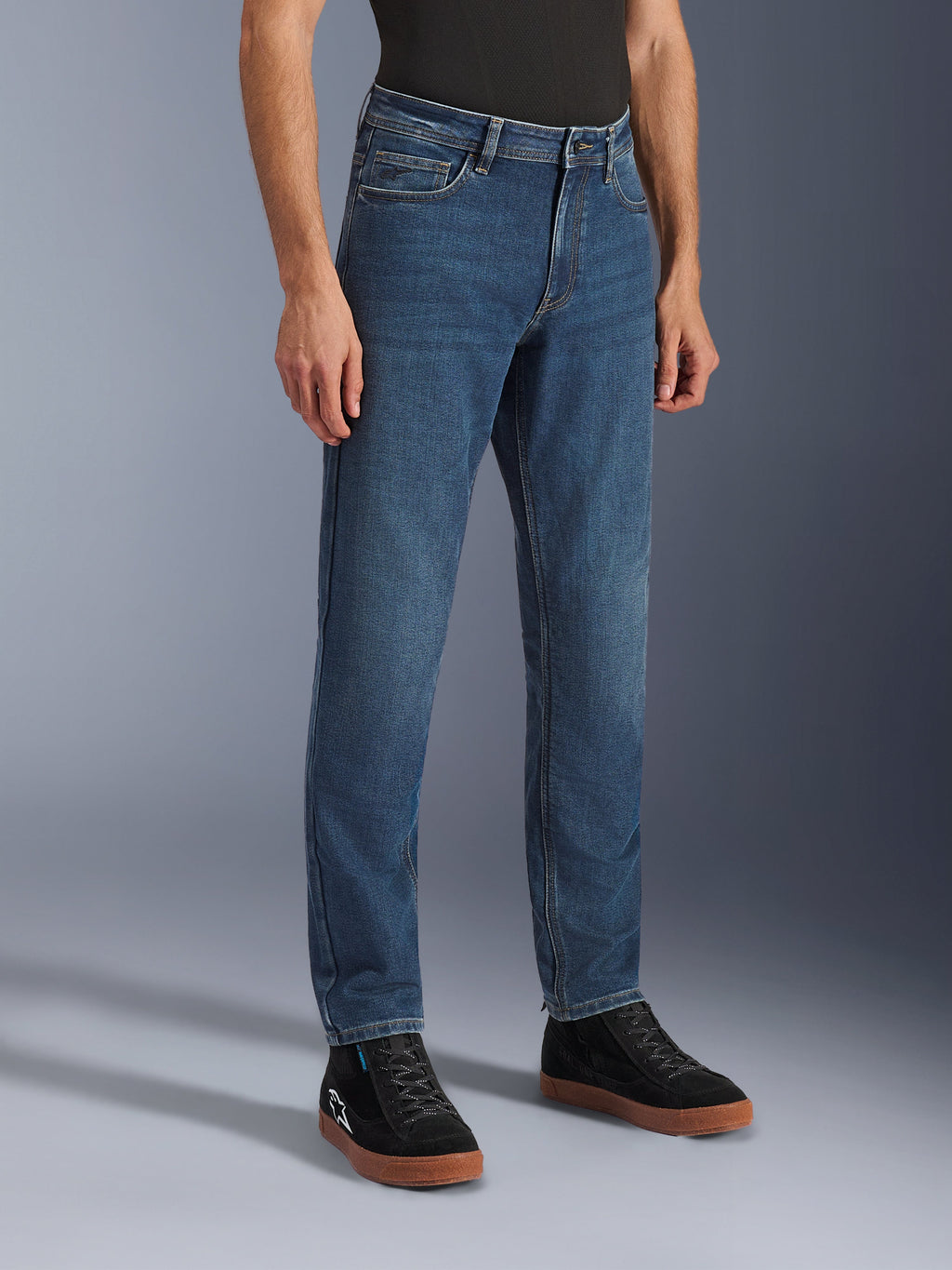 Alpinestars Flex-AST 5 Denim bukser, Indigo Washed motorcykeljeans, regular tapered fit, båret med sorte high-top sneakers og en sort trøje, afslappet urbant køreudstyr med et klassisk denim-udseende.