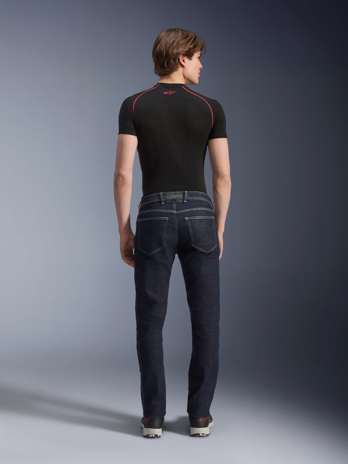 Alpinestars Copper V3 Denim bukser i Rinse Blue, urbane motorcykeljeans set bagfra, med lige ben og regular pasform, baglommer, båret med en sort kortærmet top og sneakers.