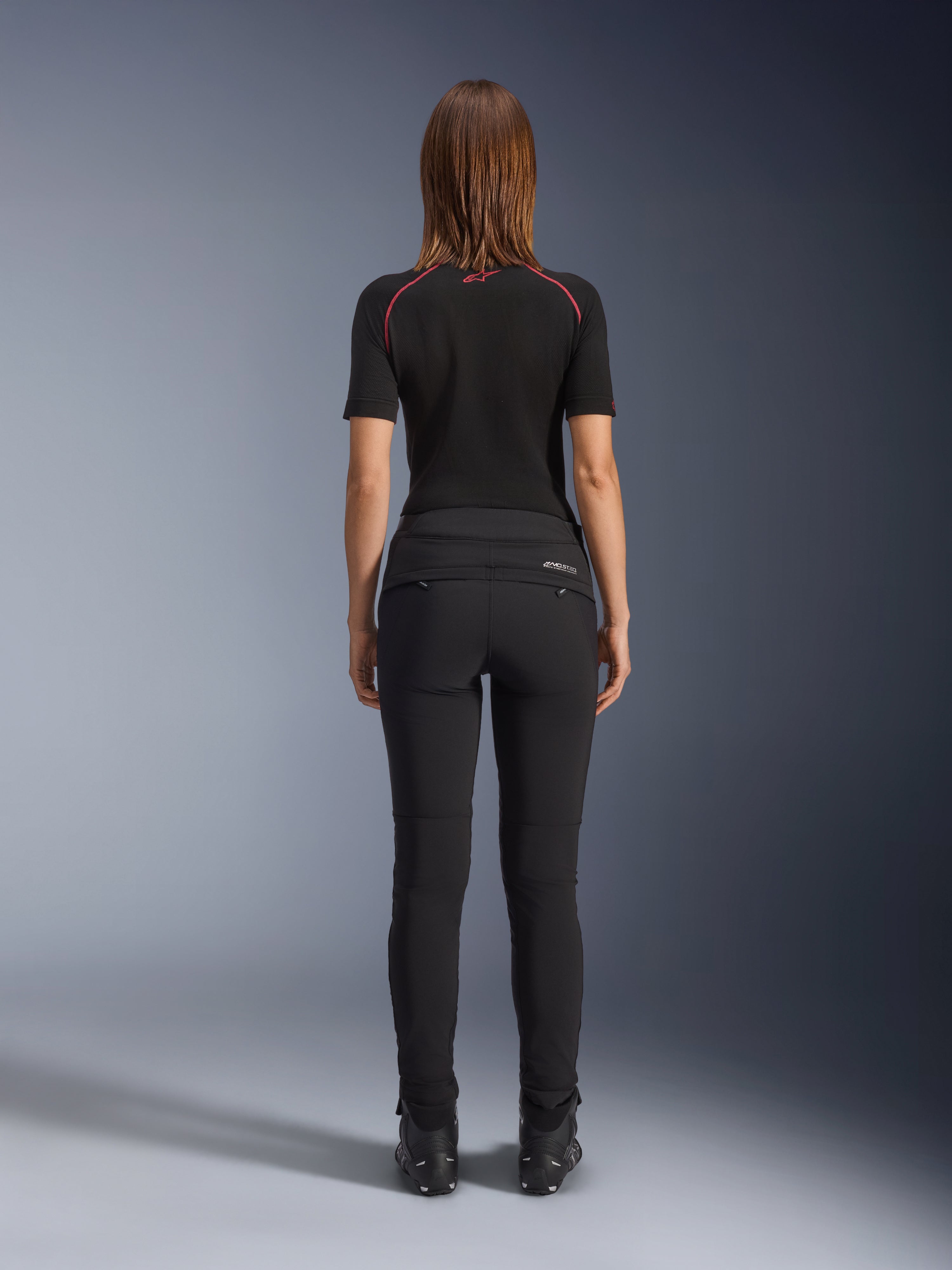 Alpinestars Alamosa Women's bukser, sort, set bagfra, tætsiddende tekstilkonstruktion, baglommer med lynlås og reflekterende MO.ST.EQ.-branding på bagstykket, båret med sort kortærmet baselayer og sorte motorcykelstøvler
