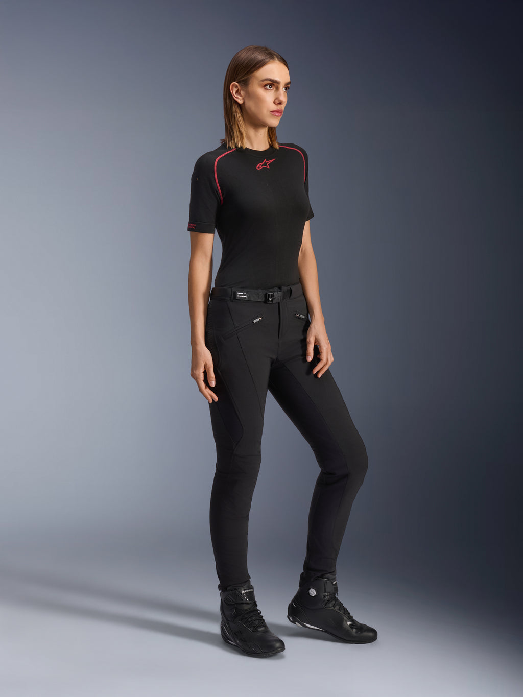 Alpinestars Alamosa damebukser, slim-fit motorcykelbukser i sort, bæres af en model med et sort basislag og køre-sko, med lynlåslommer foran og et taljebælte med magnetisk lukning, urban streetwear-stil.