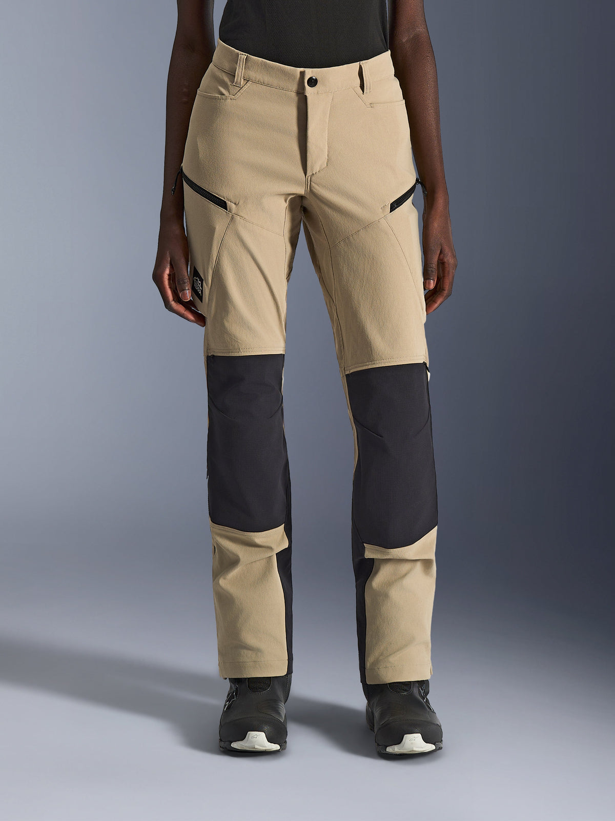 Alpinestars Woman Stella Flex-AST Explorer Pants, Women's Motorcycle Pants, Aluminum Black, front view on model, featuring sandy tan fabric with prominent black ripstop panels on the knees and lower legs, zippered pockets, adventure touring style