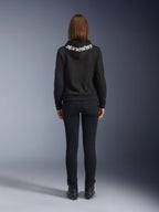 Alpinestars Daisy V3 kørejeans til damer, Black Rinse, slim fit motorcykelbukser, set bagfra med fokus på den høje talje og feminine silhuet, kombineret med en sort Alpinestars hættetrøje og sorte kørestøvler, urbant og afslappet køreudstyr