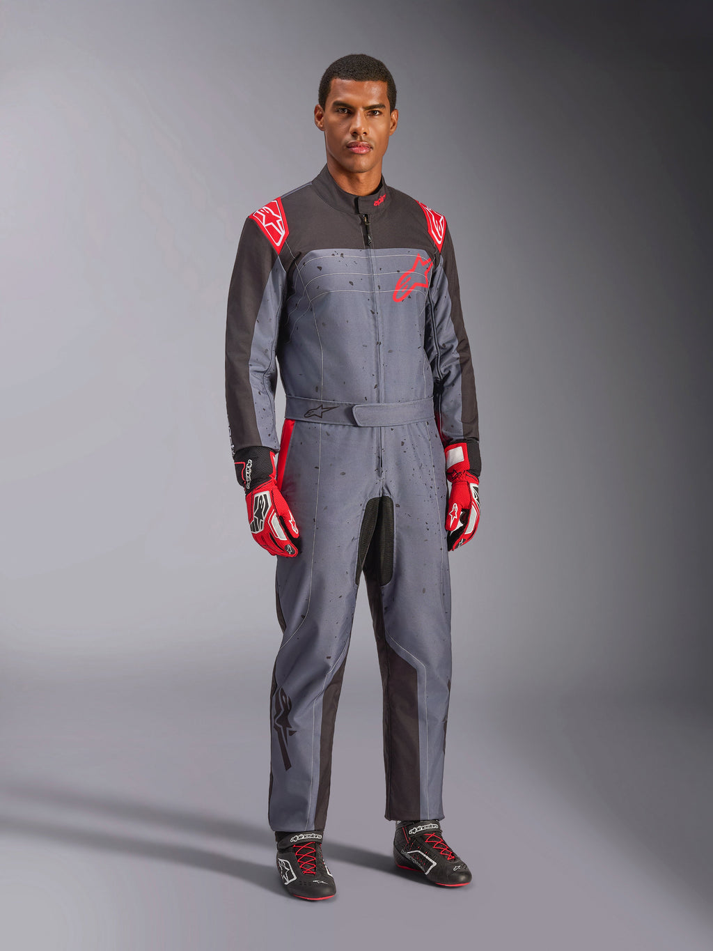 Alpinestars KMX-9 V3 Graphic 6 gokartdragt, grå og antracit med røde detaljer, unik splash-grafik på brystet og benene, kombineret med røde racerhandsker og sorte gokartsko, studieoptagelse i fuld figur.