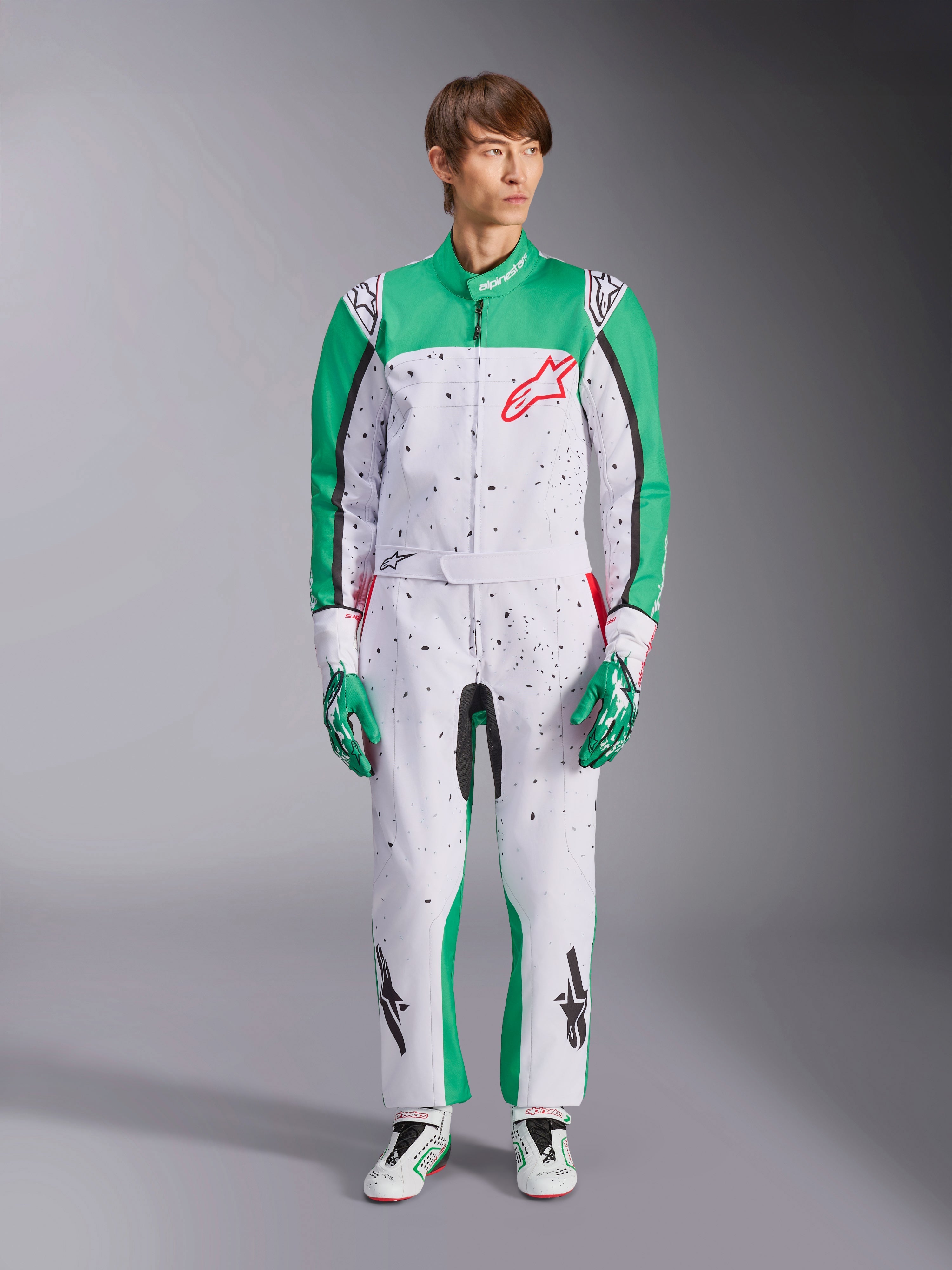 Alpinestars KMX-9 V3 Graphic 6-dragt, hvid, grøn og rød, gokart-heldragt med sort splatter-grafik, grønne paneler på ærmer og ben, rødt Alpinestars-logo på brystet, båret med matchende kørehandsker og racersko