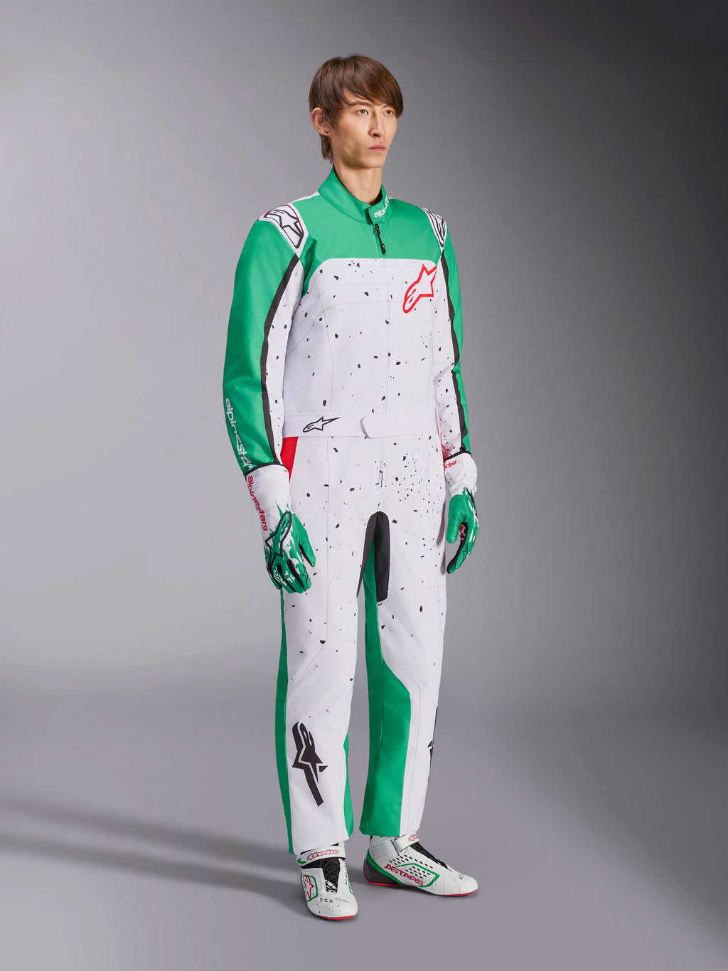 Alpinestars KMX-9 V3 Graphic 6 dragt, kartingdragt, hvid, grøn og rød, båret med matchende racerhandsker og sko, har en hvid krop med grønne ærmer og sort splatter-grafik, rødt Alpinestars-logo på brystet, atletisk heldragtsdesign til motorsport.