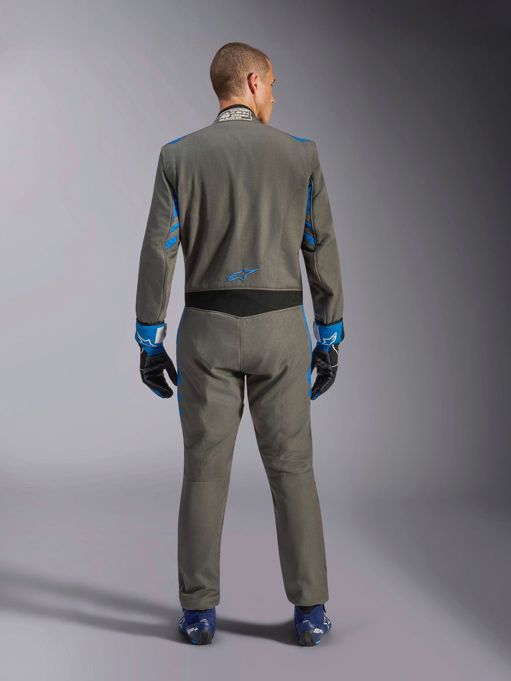 Alpinestars GP Race V3 Køredragt FIA, set bagfra, antracitblå med livlige blå detaljer på arme og skuldre, med blåt stjernelogo på lænden, båret med matchende racerhandsker og blå sko, professionel racerdragt
