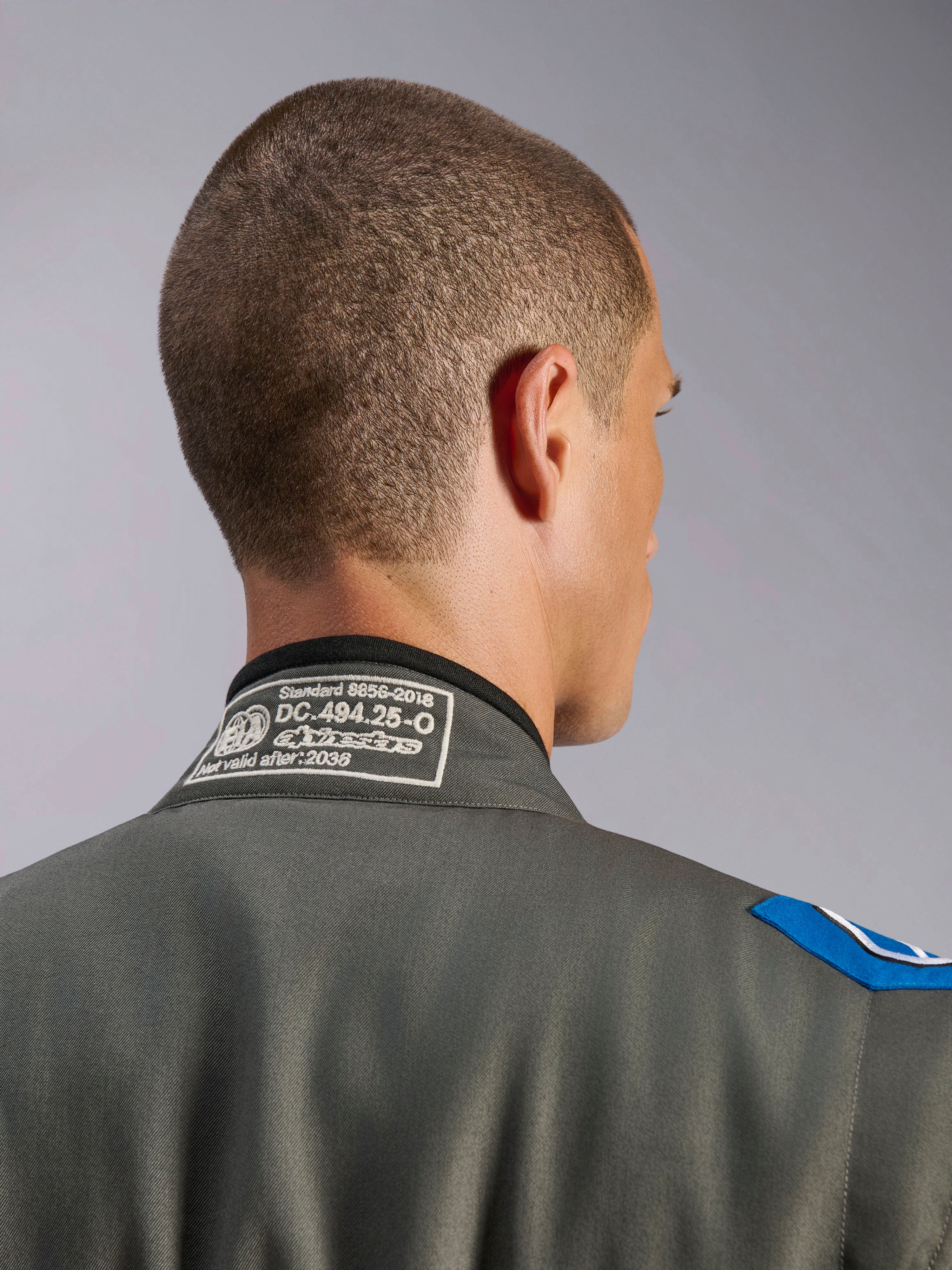 Alpinestars GP Race V3 Suit FIA i Anthracite Blue, detaljeret visning af kraven bagfra med hvidt FIA 8856-2018 homologeringslabel, tekstilkonstruktion med blå skulderaccent