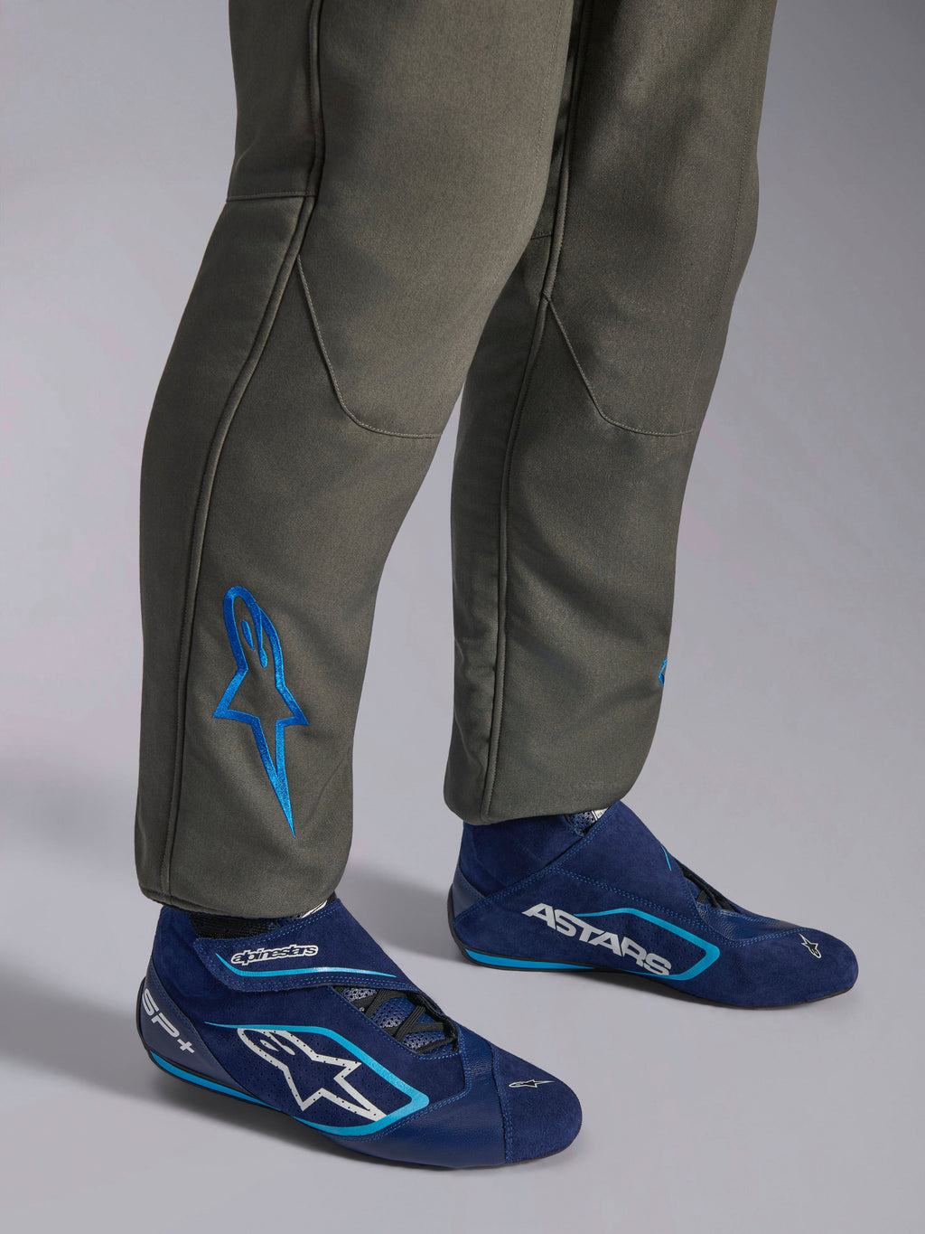 Alpinestars GP Race V3 Køredragt FIA, Anthracite Blue bilsportskøredragt, nærbillede af underben med et blåt broderet Astars-logo ved anklen, kombineret med navy- og cyanfarvede kørestøvler, professionelt beskyttelsesudstyr til motorsport