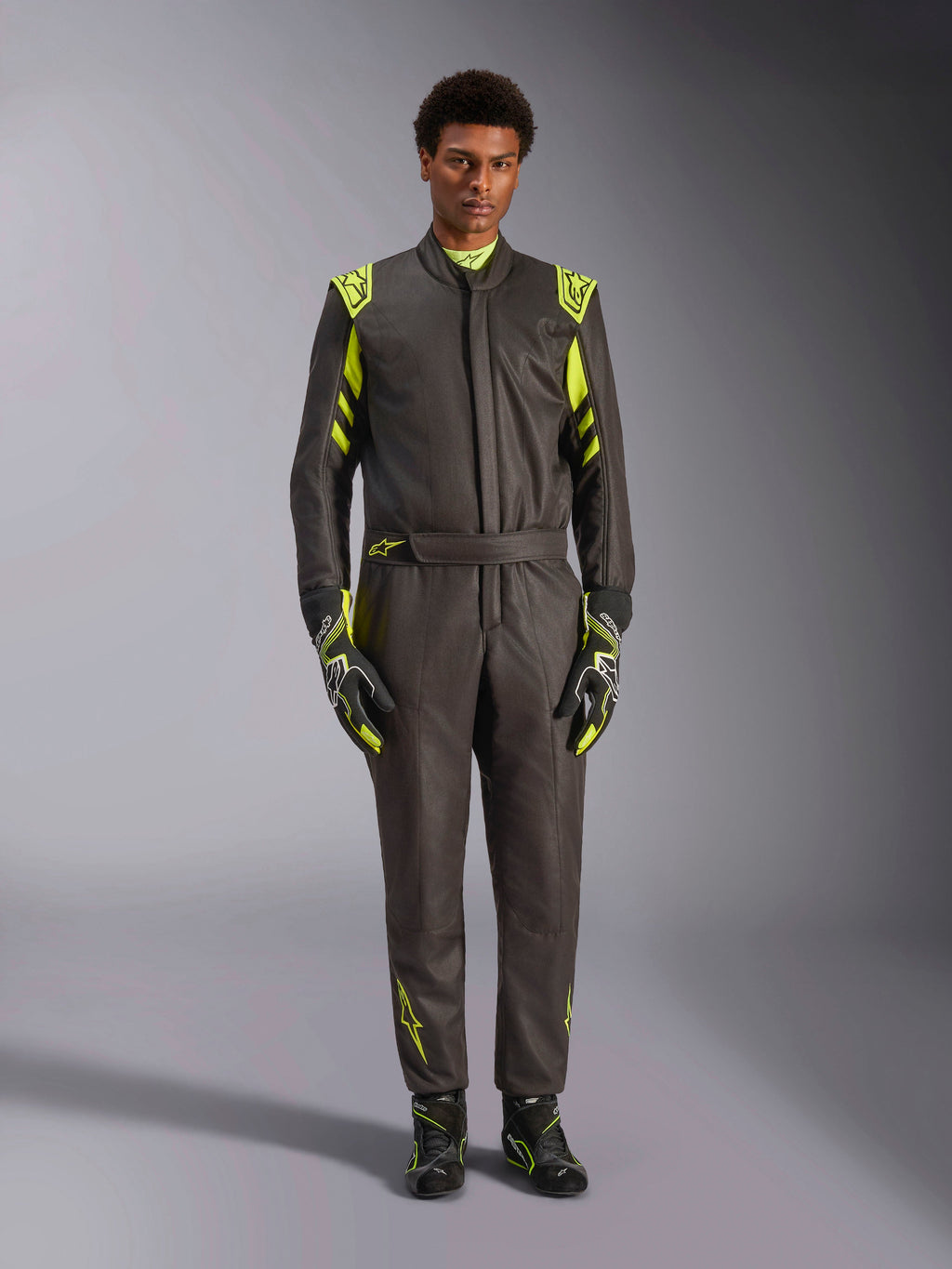 Alpinestars GP Race V3 dragt FIA, autoracerdragt, sort og fluorescerende gul, bæres af en model med matchende racerhandsker og støvler, med klare gule detaljer på skuldre, talje og ærmer, professionelt motorsportudstyr