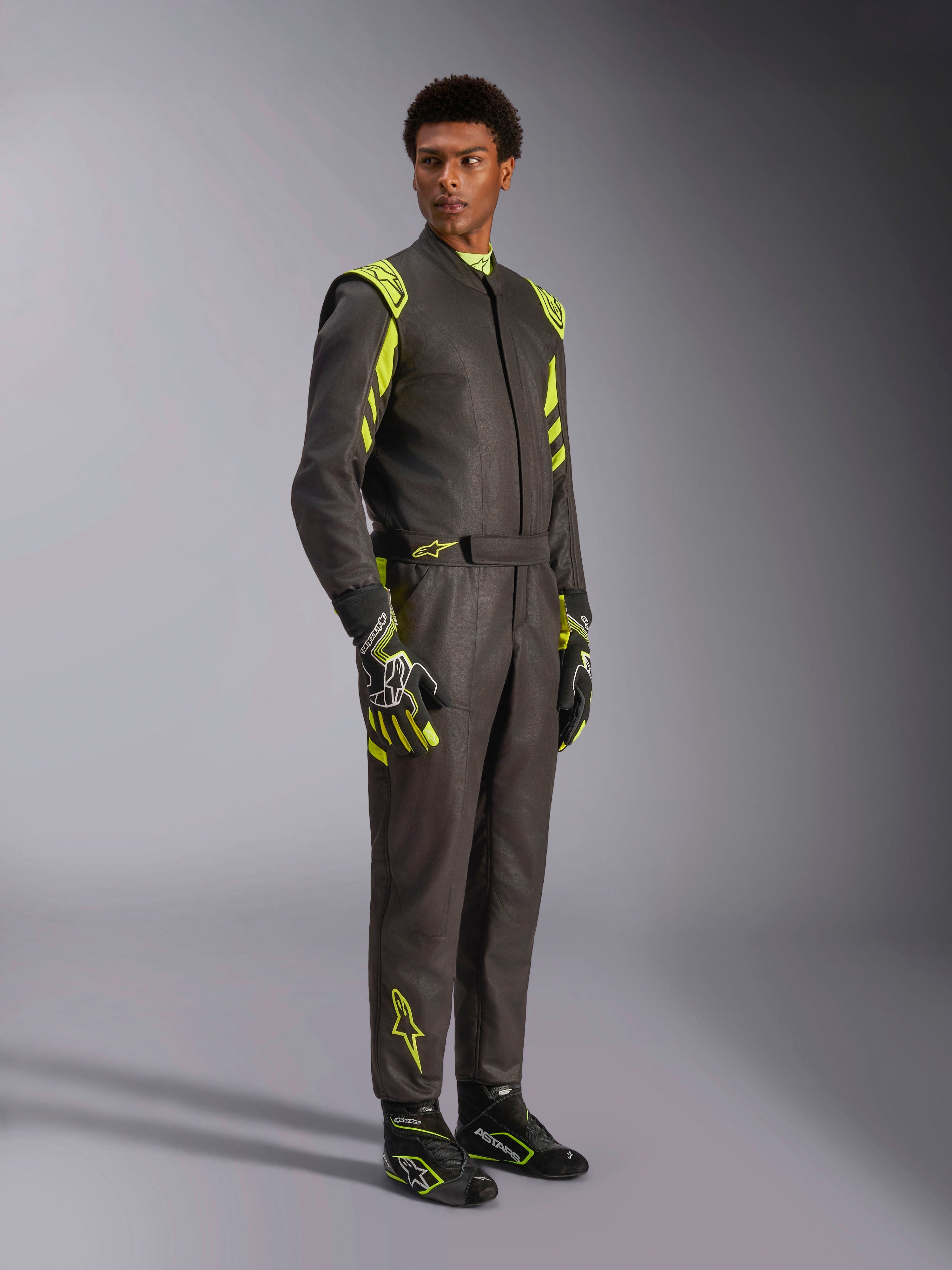 Alpinestars GP Race V3 Køredragt FIA, bilvæddeløbsdragt, sort og neongul, båret af en model med matchende racerhandsker og støvler, med markante gule detaljer på skuldre og ben, professionelt motorsportudstyr