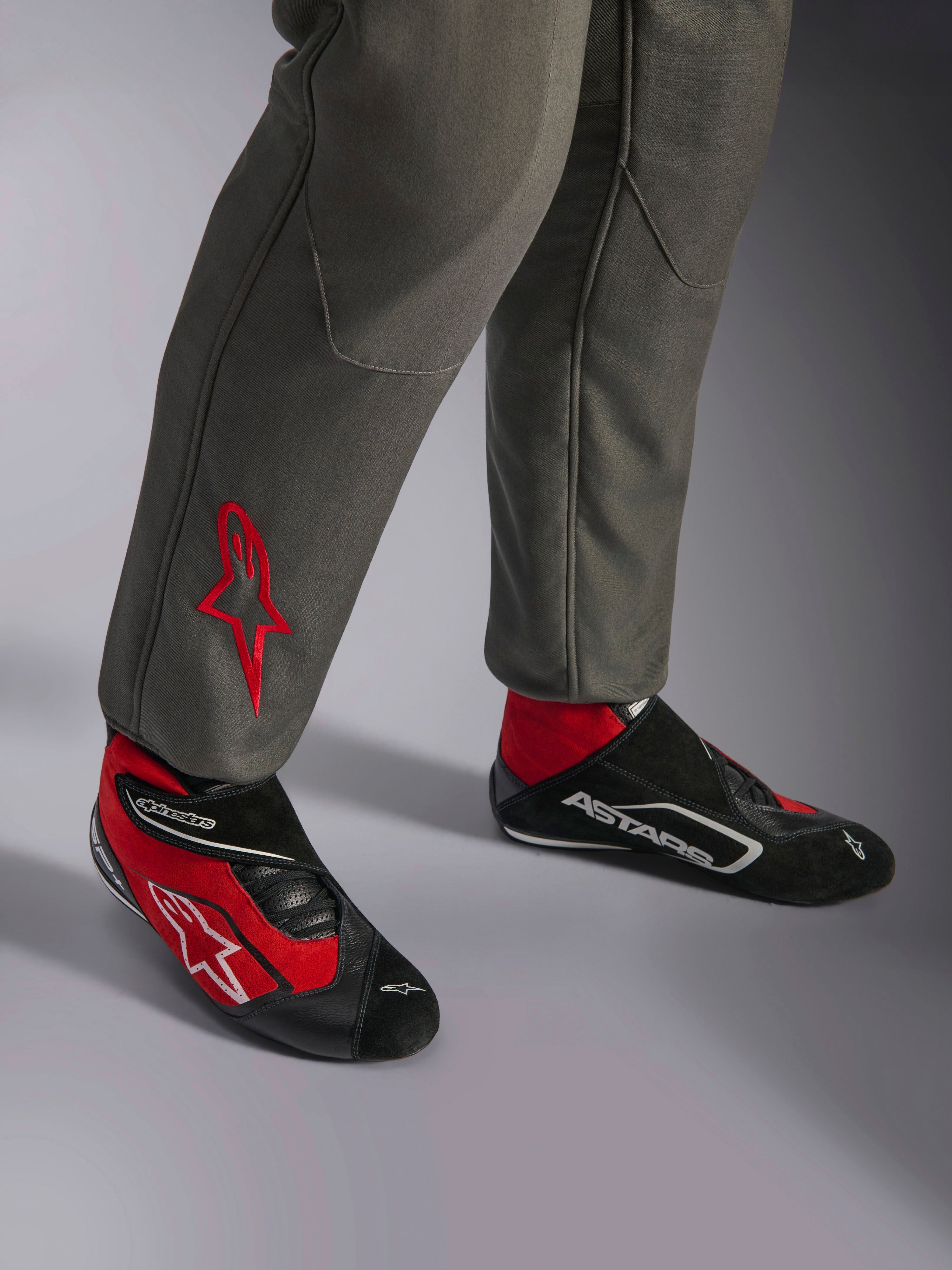 Alpinestars GP Race V3 Suit FIA, Anthracite Red-køredragt, nærbillede af underben med broderet rødt stjernelogo, kombineret med røde og sorte racestøvler, professionelt bilsportsudstyr designet til førerbeskyttelse og komfort