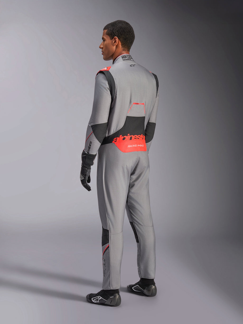 Alpinestars Hypertech V3-dragt i Mid Gray Black Red Fluo, set bagfra i trekvart profil, med markant rød Alpinestars-branding på lænden, sorte strækpaneler og en slank atletisk pasform til professionel autoracing.