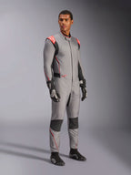 Mandlig model iført Alpinestars Hypertech V3-dragt i Mid Gray med sorte og rød fluo-detaljer, professionel autoracerdragt kombineret med sorte racerhandsker og -sko, med en letvægts to-lags Nomex-konstruktion, røde skulderdetaljer og en atletisk pasform