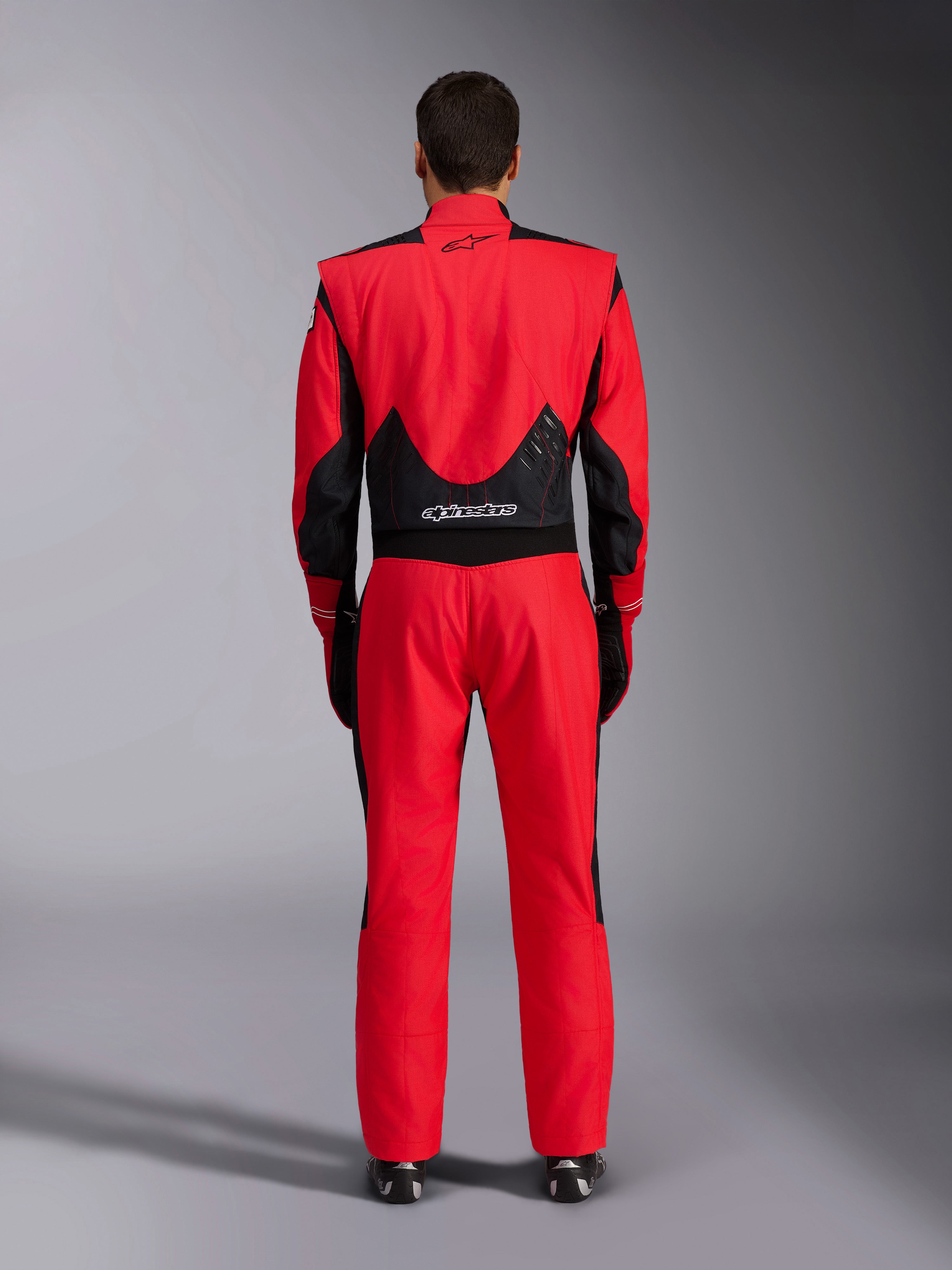 Alpinestars GP Pro Comp V2 FIA køredragt, rød og sort, set bagfra med sorte mesh- og strækpaneler på lænden, Alpinestars-branding på øvre og nedre del af ryggen, professionelt autoracingudstyr