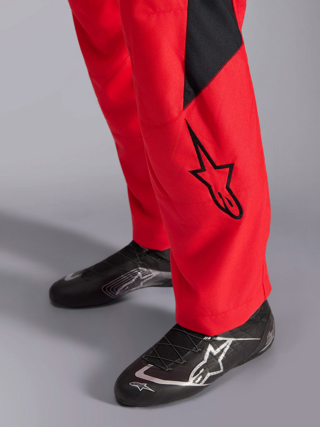 Alpinestars GP Pro Comp V2 FIA køredragt, nærbillede af underbenet og køresko, rød med sort Astars-logo og panel, kombineret med sort performance kørefodtøj, bilsportsudstyr
