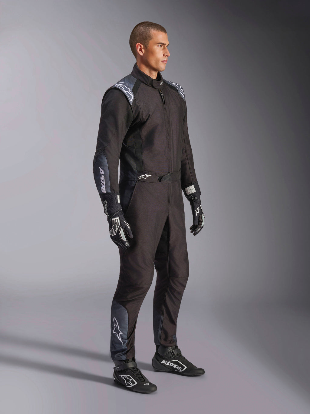 Alpinestars KMX-5 V3 dragt, kartingdragt i Black Dark Shadow, båret med matchende sorte racerhandsker og sko, med laserskårne perforeringer og tekniske mesh-paneler, strømlinet dobbeltlagskonstruktion med hvid branding til professionel motorsport