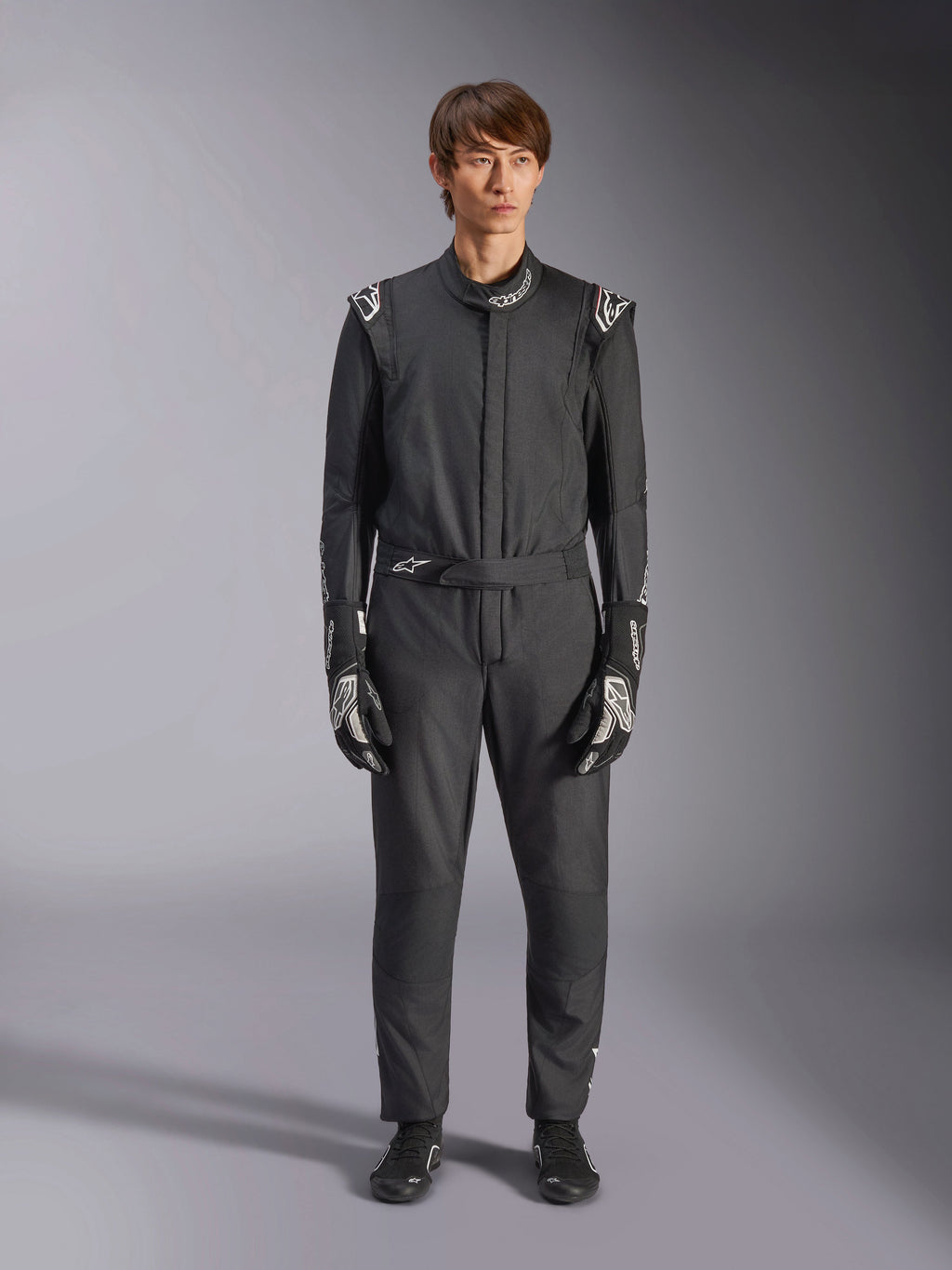 Alpinestars GP Tech V4 Suit, Black and White, professional one-piece auto racing suit, worn with matching black and white gloves and racing shoes, featuring white Alpinestars logos on shoulders and collar, sleek athletic fit for motorsport competition