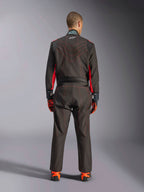 Rear view of a driver wearing the Alpinestars KMX-9 V3 Suit, Karting Suit, Black with Red Fluo accents and red contrast stitching, professional motorsport racing gear, worn with orange and black racing gloves and shoes.