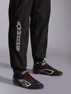 Alpinestars KMX-9 V3 dragt, kartingdragt, sort og hvid, detalje af underben med stort hvidt Alpinestars-branding, båret med sorte og røde racerstøvler, professionelt motorsportudstyr til karting